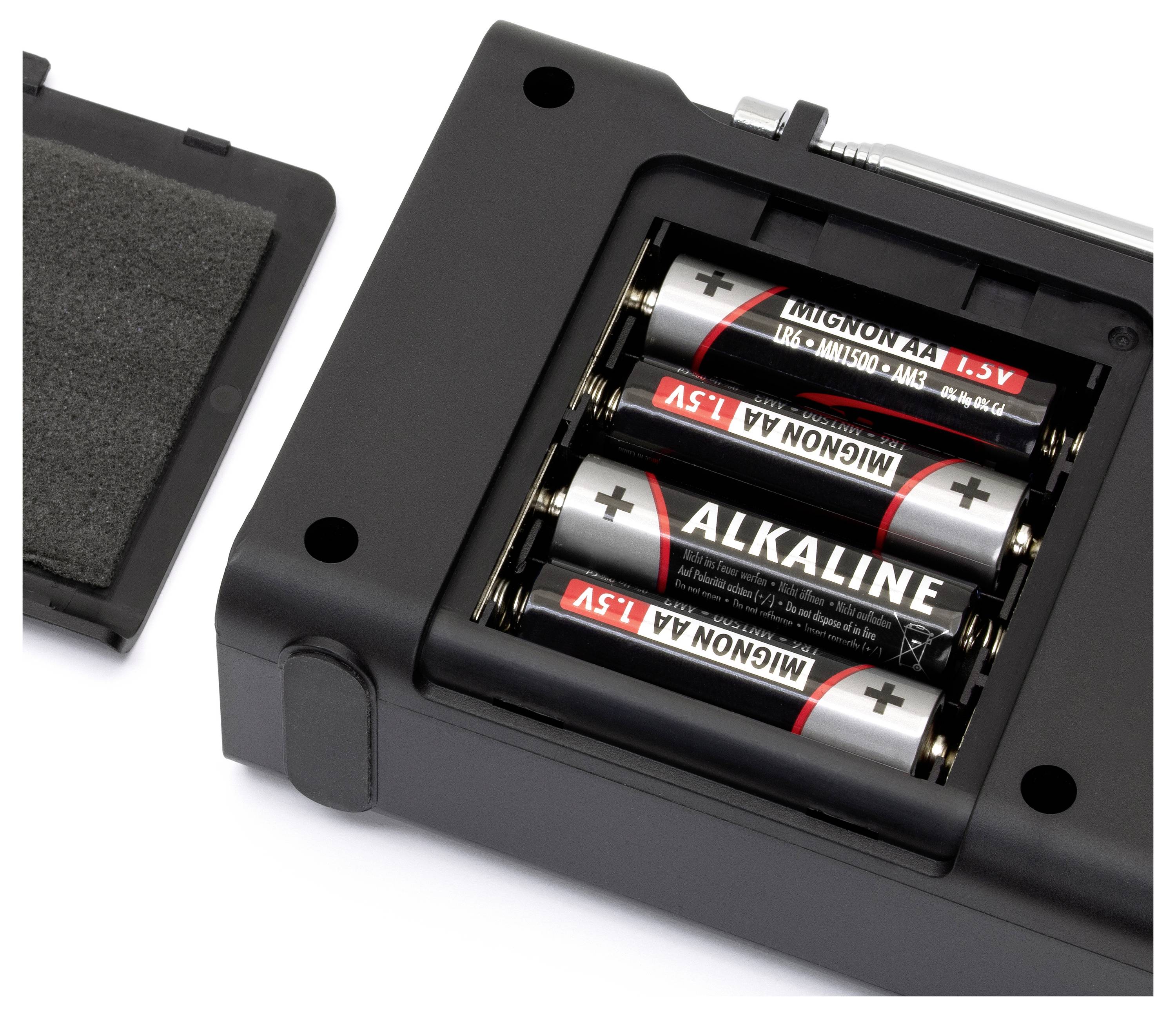 Ein Batteriefach mit vier AA-Alkalibatterien, die korrekt eingesetzt sind. Links ist der entfernte Batteriefachdeckel zu sehen.