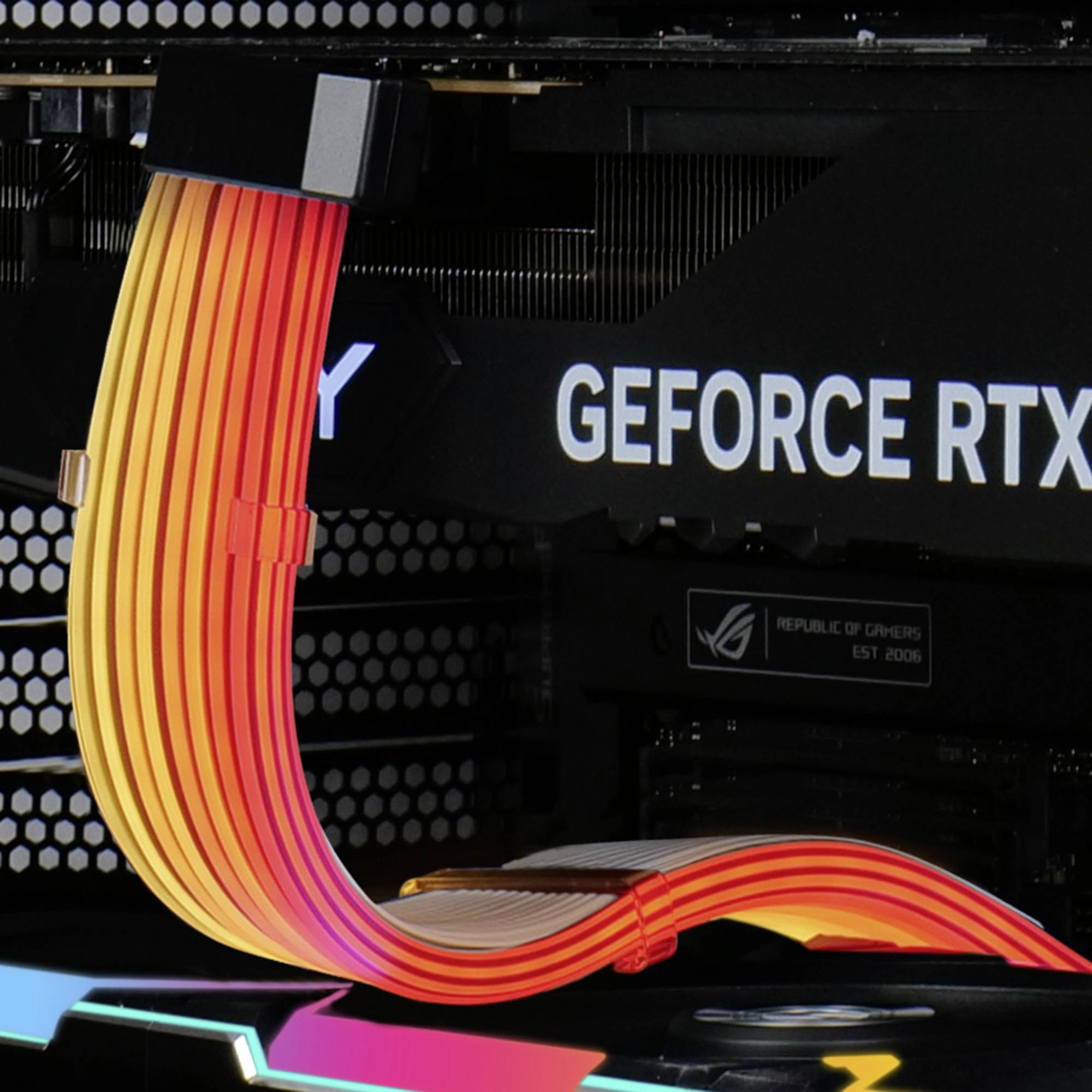 Eine bunte PCIe-Stromverlängerung führt zu einer Grafikkarte, auf der 'GEFORCE RTX' steht. Im Hintergrund sind PC-Komponenten zu sehen.