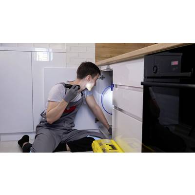 'Ein Handwerker in Arbeitskleidung repariert einen Schrank unter der Küche. Er benutzt eine Taschenlampe zur besseren Sichtbarkeit.'