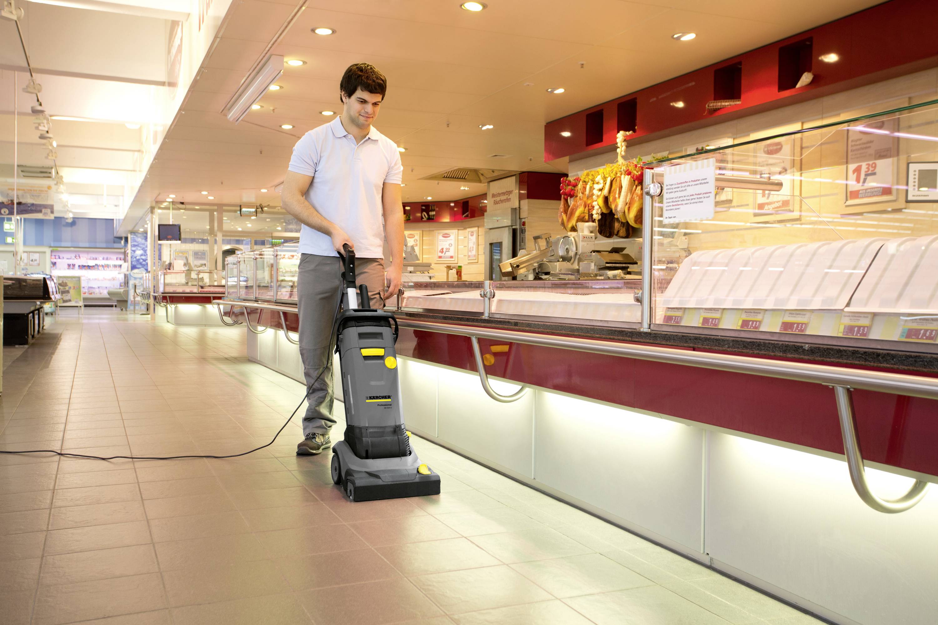 Ein Mann reinigt mit einem professionellen Bodenreinigungsgerät den Boden in einer Fleischerei, umgeben von Fleischvitrinen.