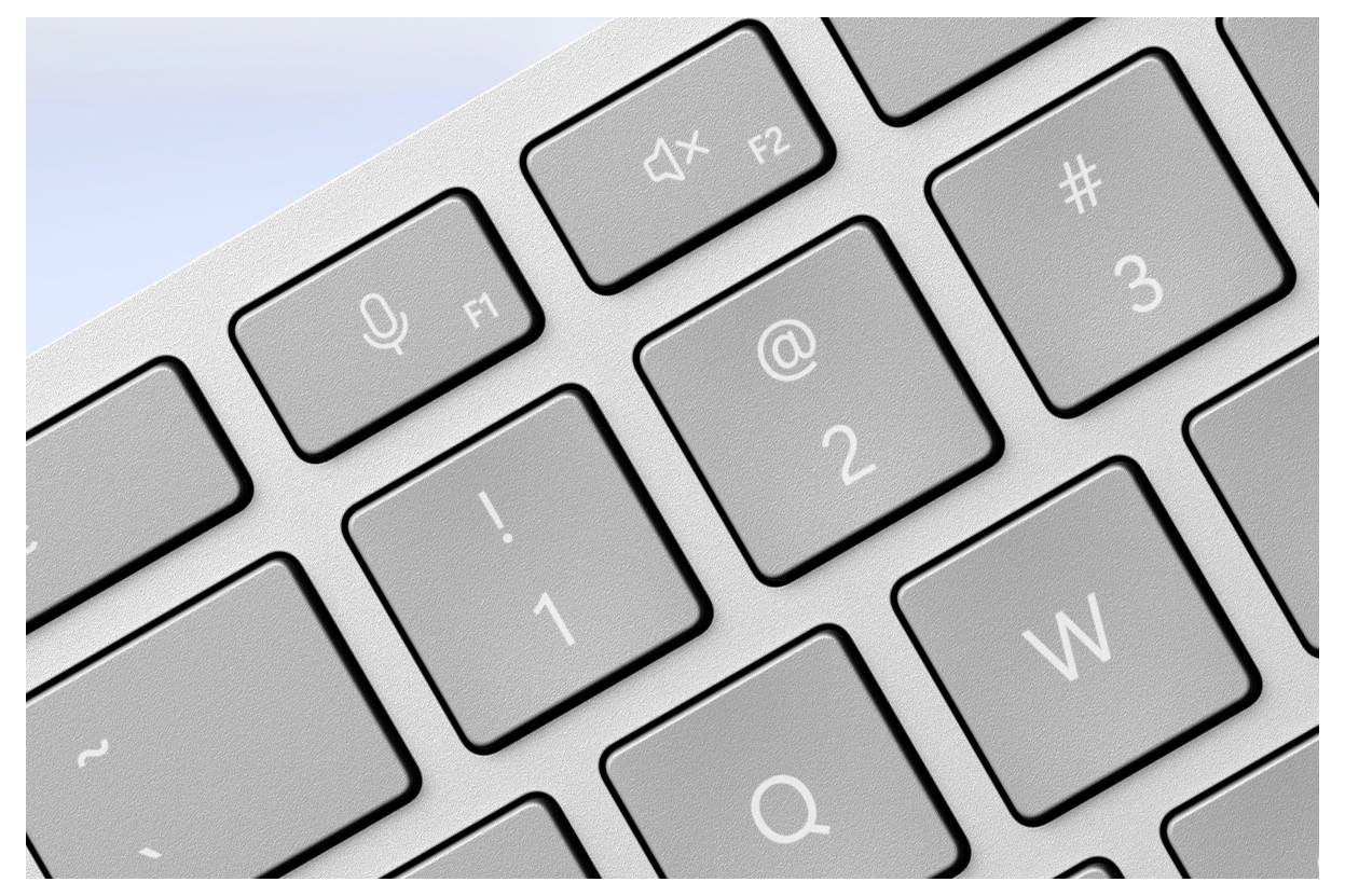 Nahaufnahme einer Computertastatur mit Mikrofon- und Lautlos-Symbolen auf den Tasten F1 und F2. Einige Zahlen- und Buchstabentasten sichtbar.