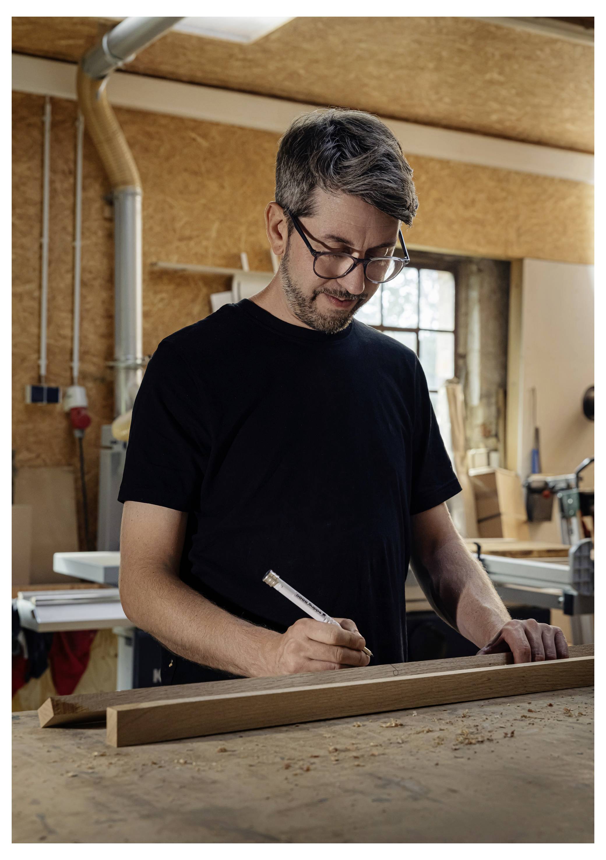 Ein Mann, der in einer Werkstatt ein Holzbrett vermisst und markiert, bereitet sich auf ein Tischlerproject vor.
