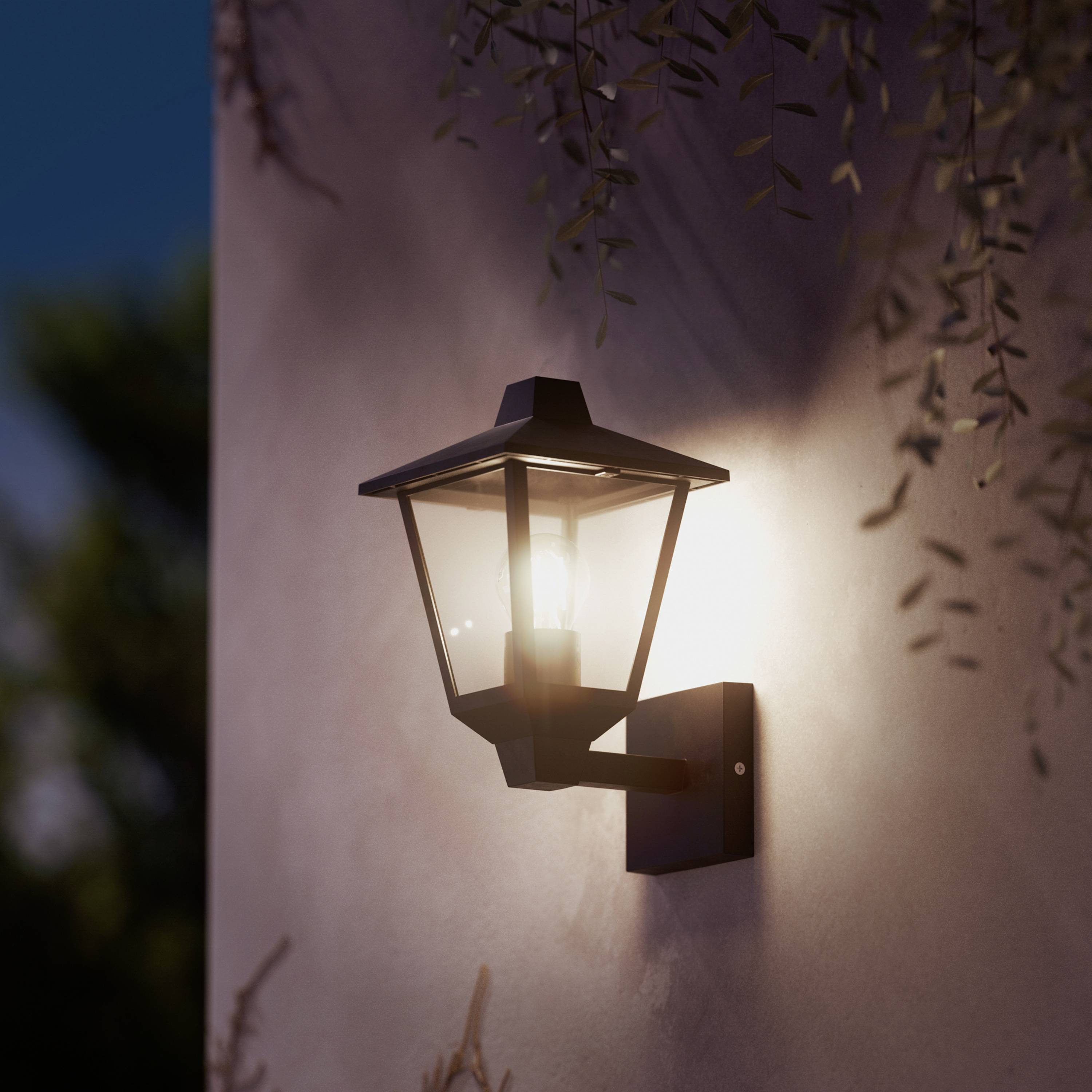 Außenlaterne an einer Wand, an einem Abend oder in der Dämmerung. Die Lampe strahlt ein warmes Licht aus und beleuchtet die Umgebung.