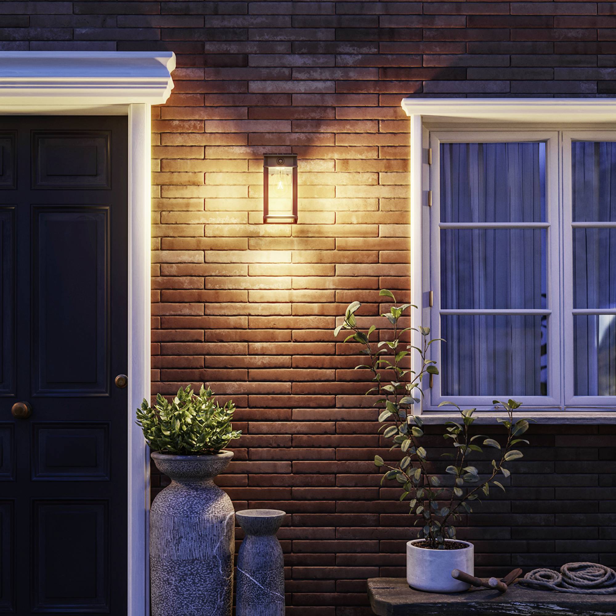 Hausfassade bei Nacht, beleuchtet von Wandlampe. Großer Blumentopf mit Grünpflanze neben einer Tür mit Fenster im traditionellen Stil.