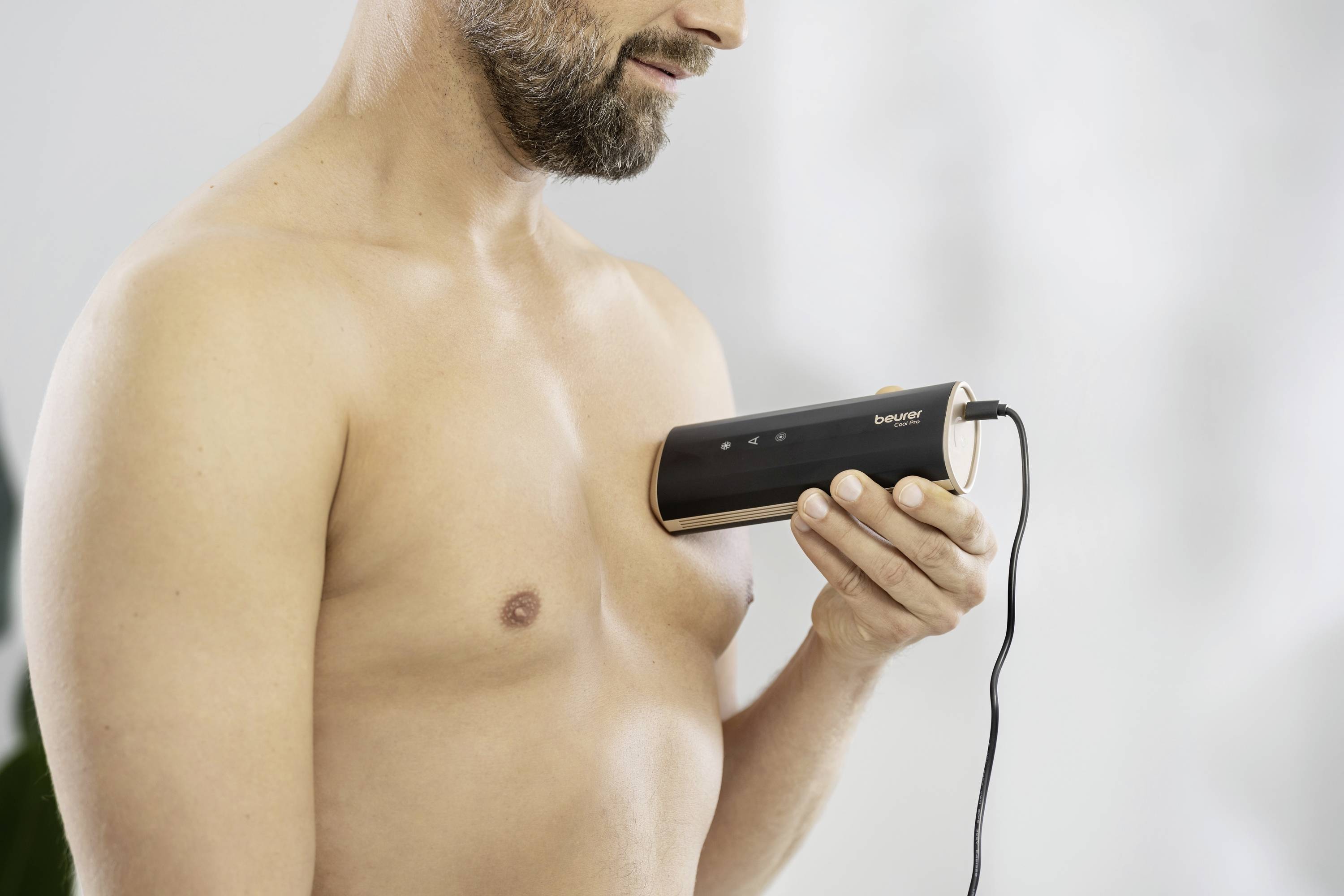 Ein Mann untersucht seine Brust mit einem drahtgebundenen medizinischen Gerät, möglicherweise zur Selbstdiagnose oder Vorsorge.