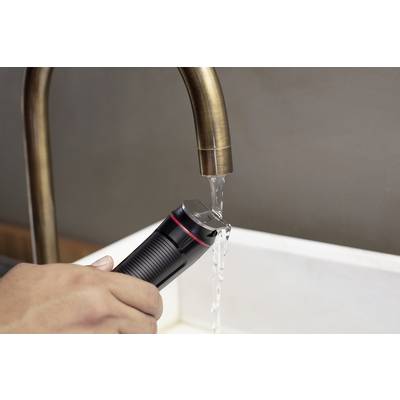 Eine Hand hält einen schwarzen elektrischen Rasierer unter einen Wasserhahn mit fließendem Wasser über einem weißen Waschbecken.