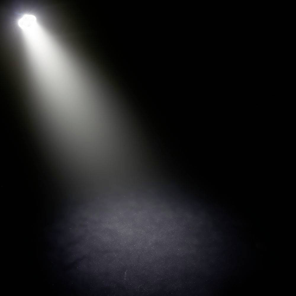 Ein einzelner heller Lichtstrahl fällt von oben auf eine dunkle Bühne und hebt einen runden Bereich hervor, umgeben von Schatten.
