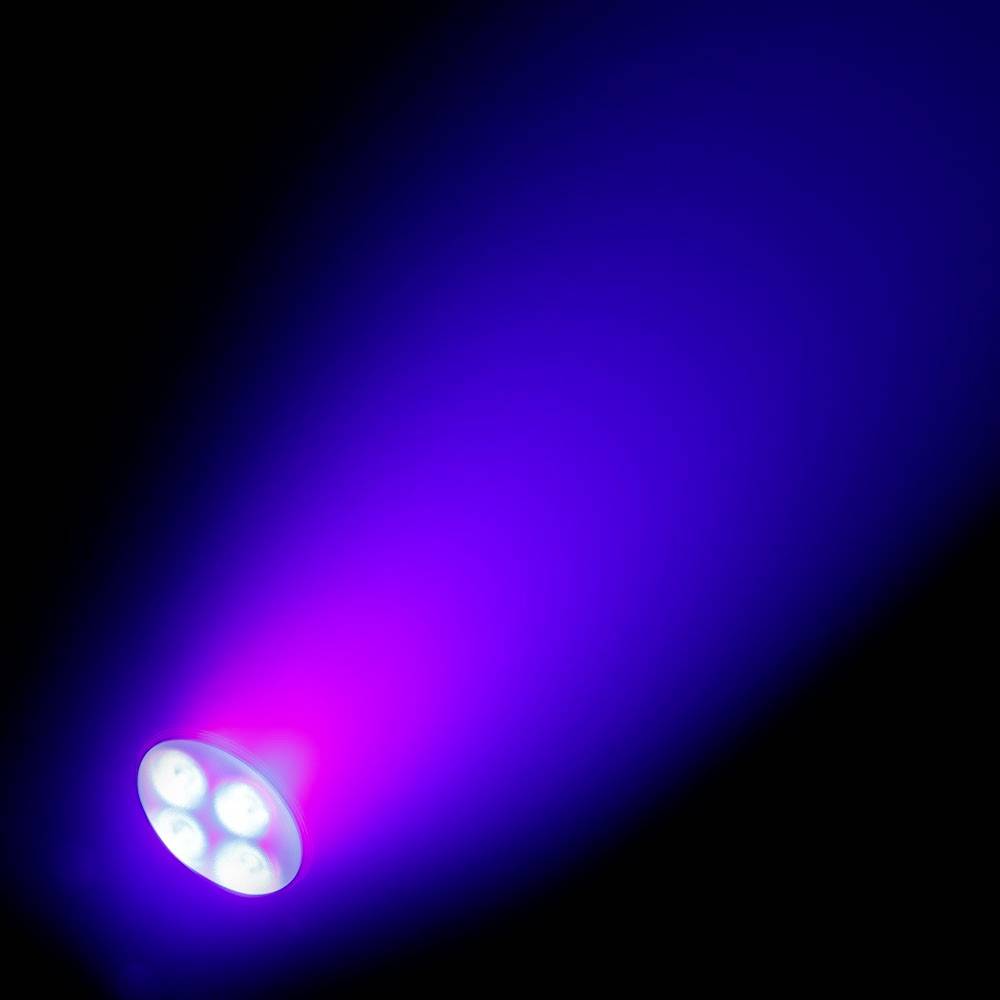 Eine LED-Lampe strahlt lila und blaues Licht in einem dunklen Raum aus, das sich in einem Kegel über den Hintergrund verteilt.