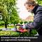 Mann in Schutzbrille schneidet eine Hecke mit elektrischer Heckenschere im Garten. Text: 'Schmaler Frontgriff mit Mikroschalter zur angenehmen Handhabung'.