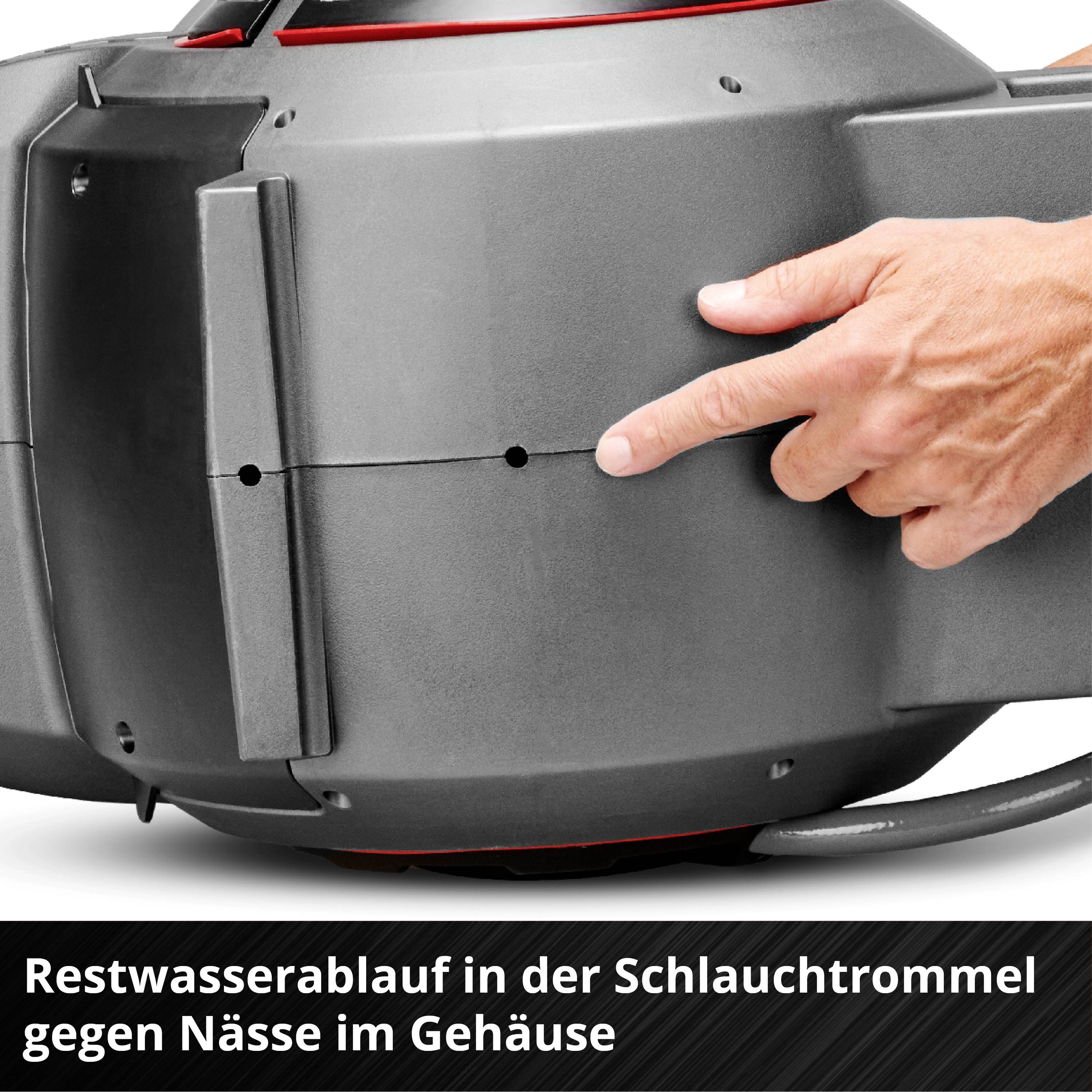 Hand justiert einen grauen Schlauchaufroller mit rotem Restwasserablauf, beschriftet mit 'Restwasserablauf in der Schlauchtrommel gegen Nässe im Gehäuse'.