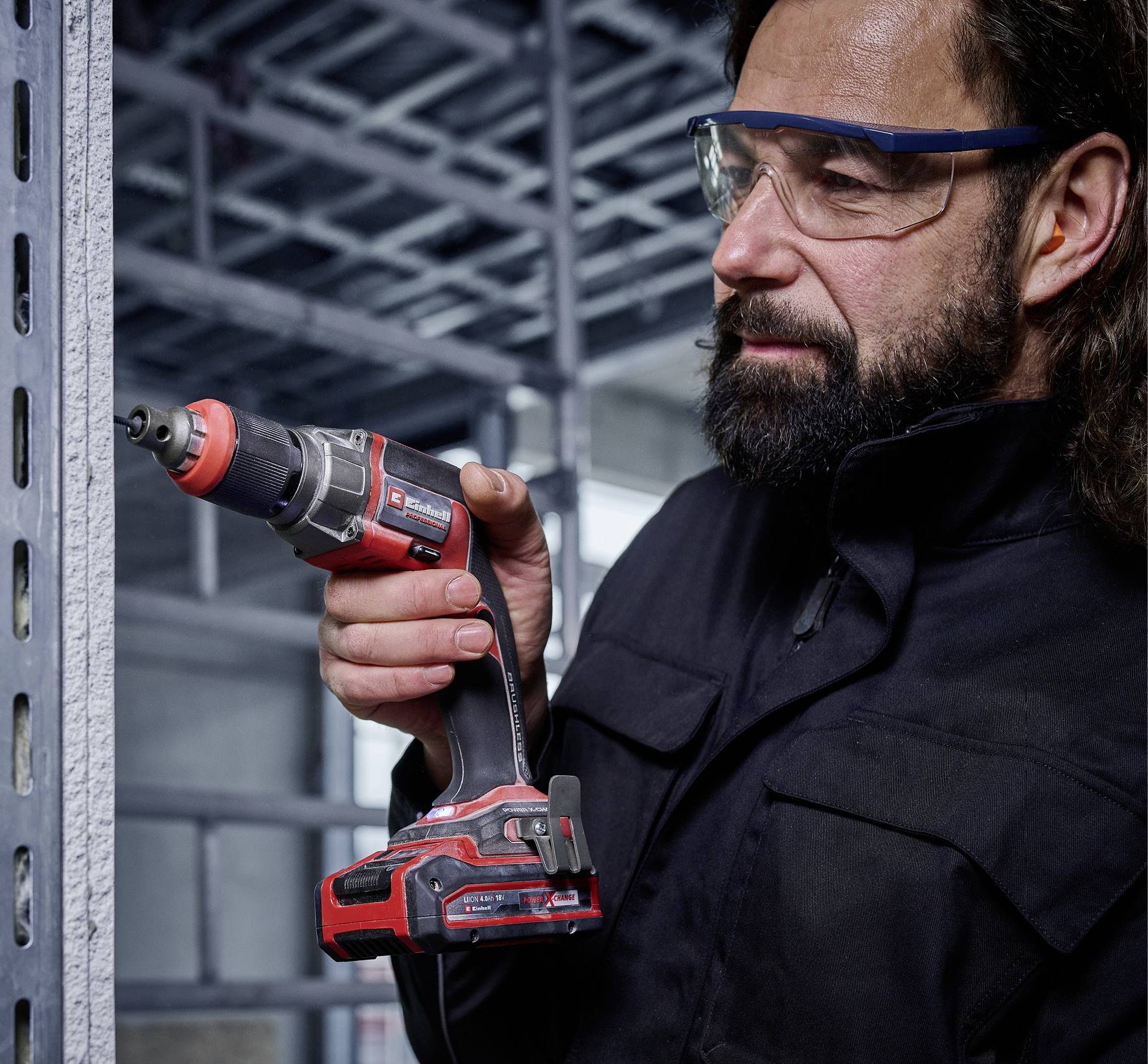 Eine Person benutzt eine elektrische Bohrmaschine, um Löcher in ein Metallschienenregal zu bohren. Sie trägt eine Schutzbrille.