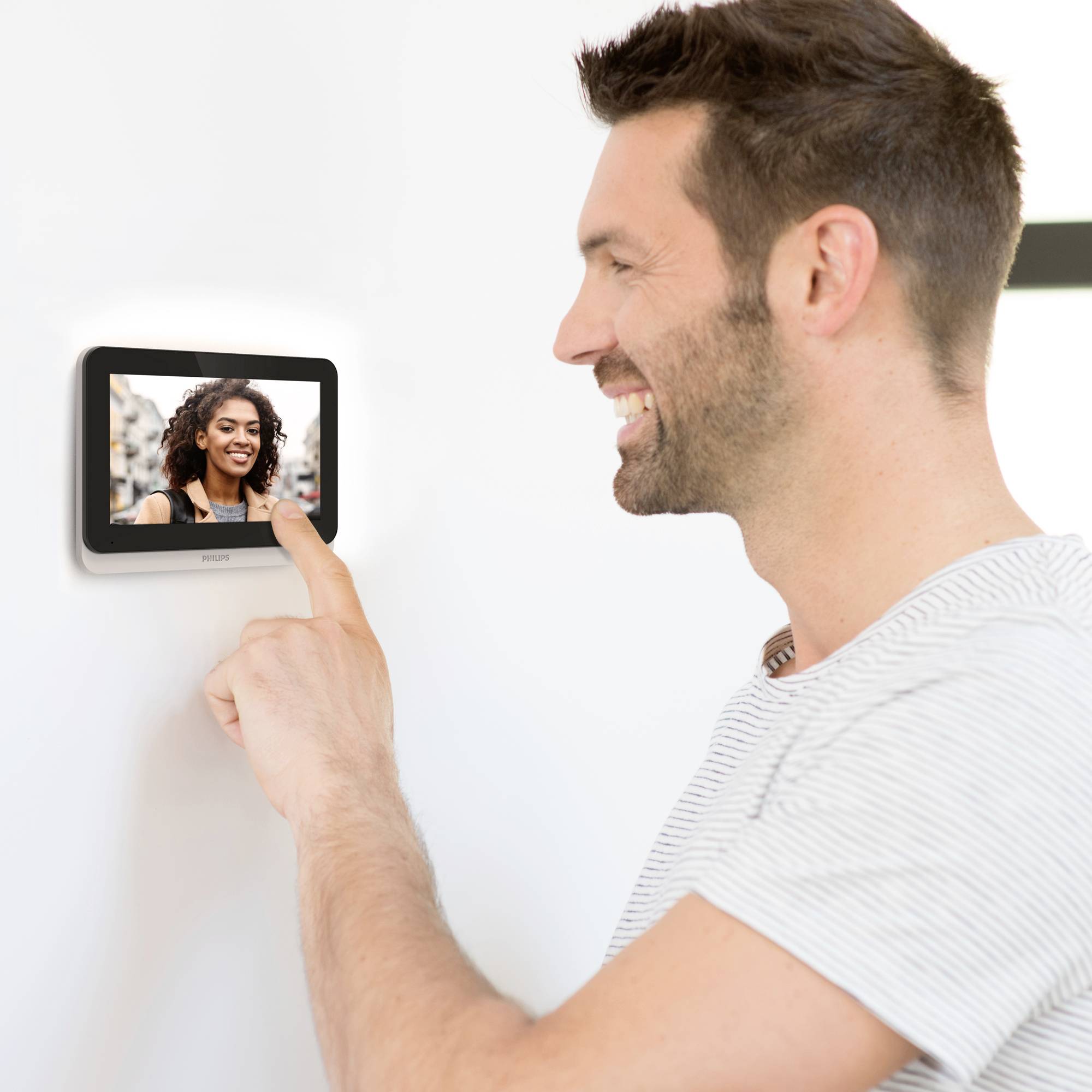 Ein Mann interagiert mit einem kleinen Bildschirm an der Wand, auf dem das Bild einer lächelnden Frau zu sehen ist.