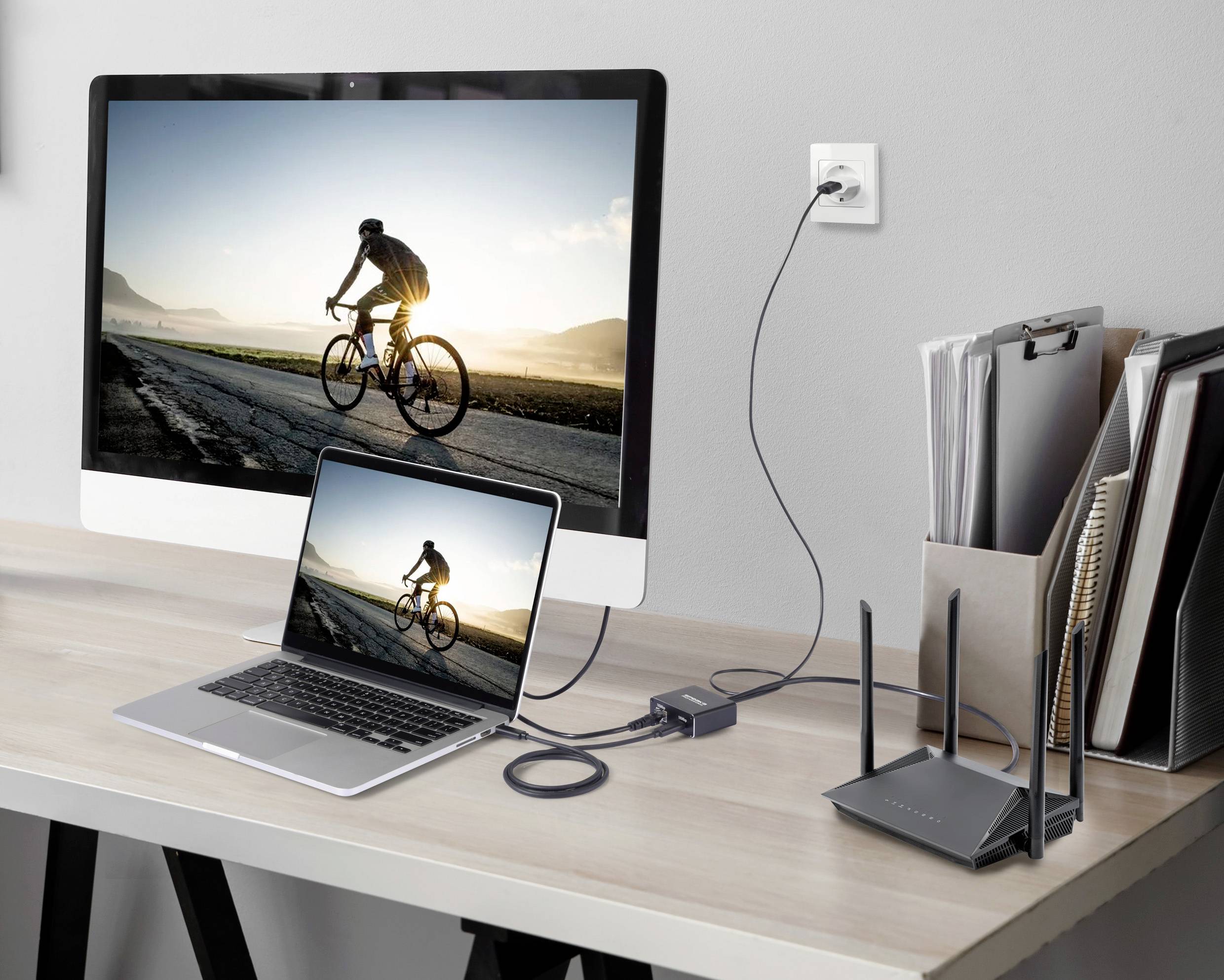 Ein Computermonitor zeigt einen Radfahrer bei Sonnenuntergang. Ein Laptop ist mit einem Router verbunden und zeigt dasselbe Bild.