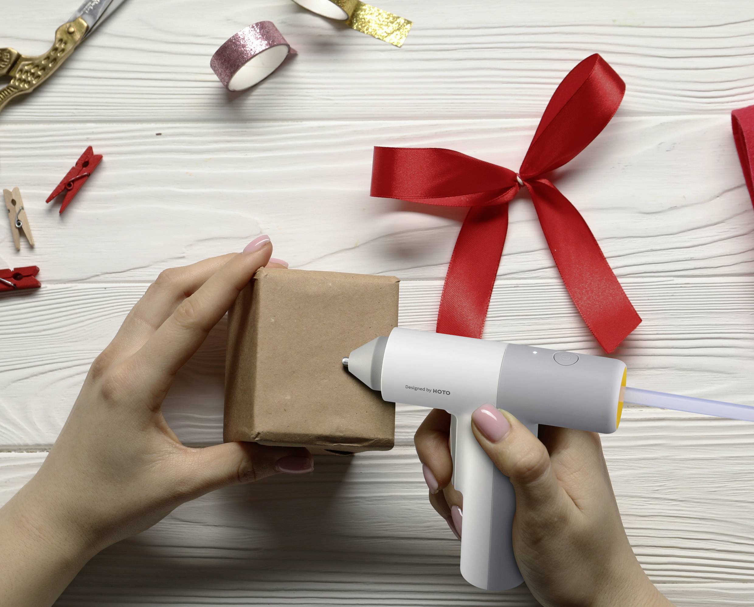 Person verpackt Geschenk mit Klebepistole und Dekobändern.