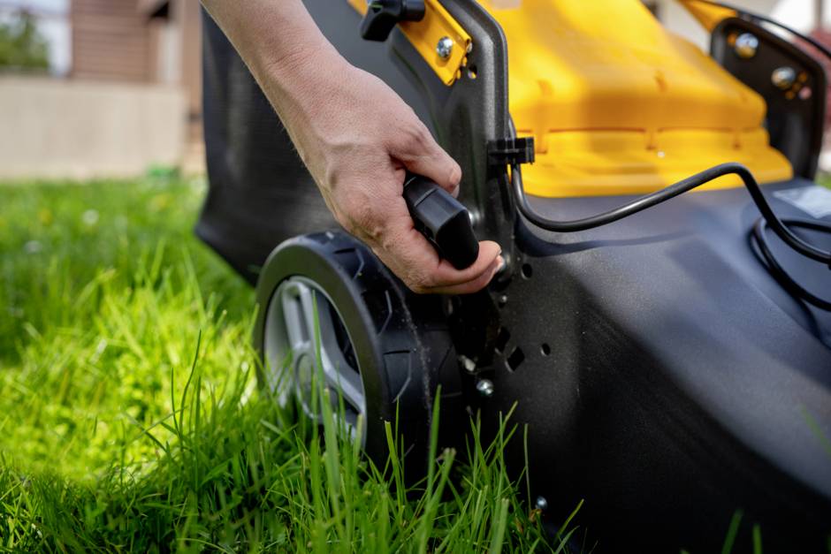 'Hand zieht den Hebel eines elektrischen Rasenmähers im Garten.'