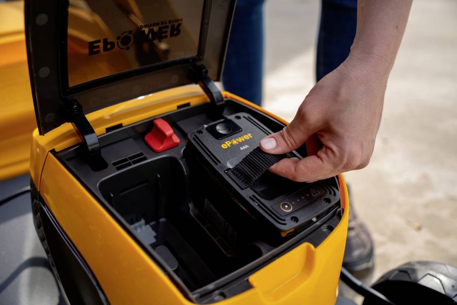 Eine Person installiert oder entfernt eine Batterie aus dem Gehäuse eines gelben Elektrogeräts.