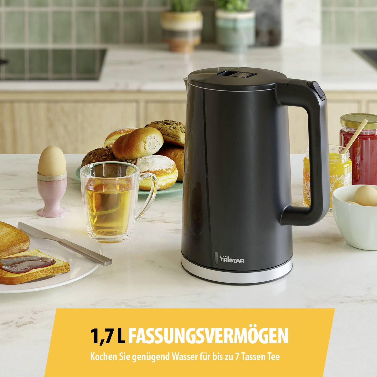 Ein Wasserkocher mit 1,7 l Fassungsvermögen steht auf einem Frühstückstisch mit Brötchen und Marmelade. Text: 'Kochen Sie genug Wasser für bis zu 7 Tassen Tee'.