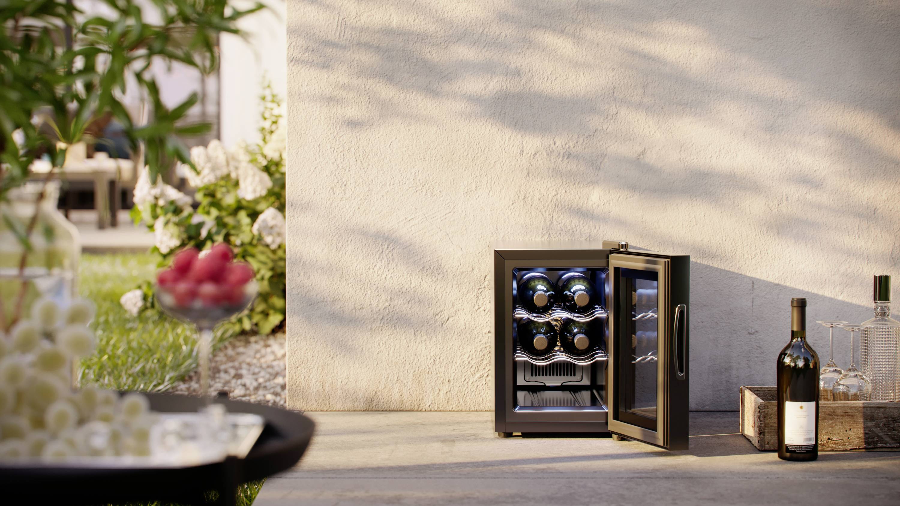 Ein geöffneter Weinkühlschrank mit Flaschen steht draußen neben einer Mauer. Im Vordergrund ein Tisch mit Trauben und Himbeeren.