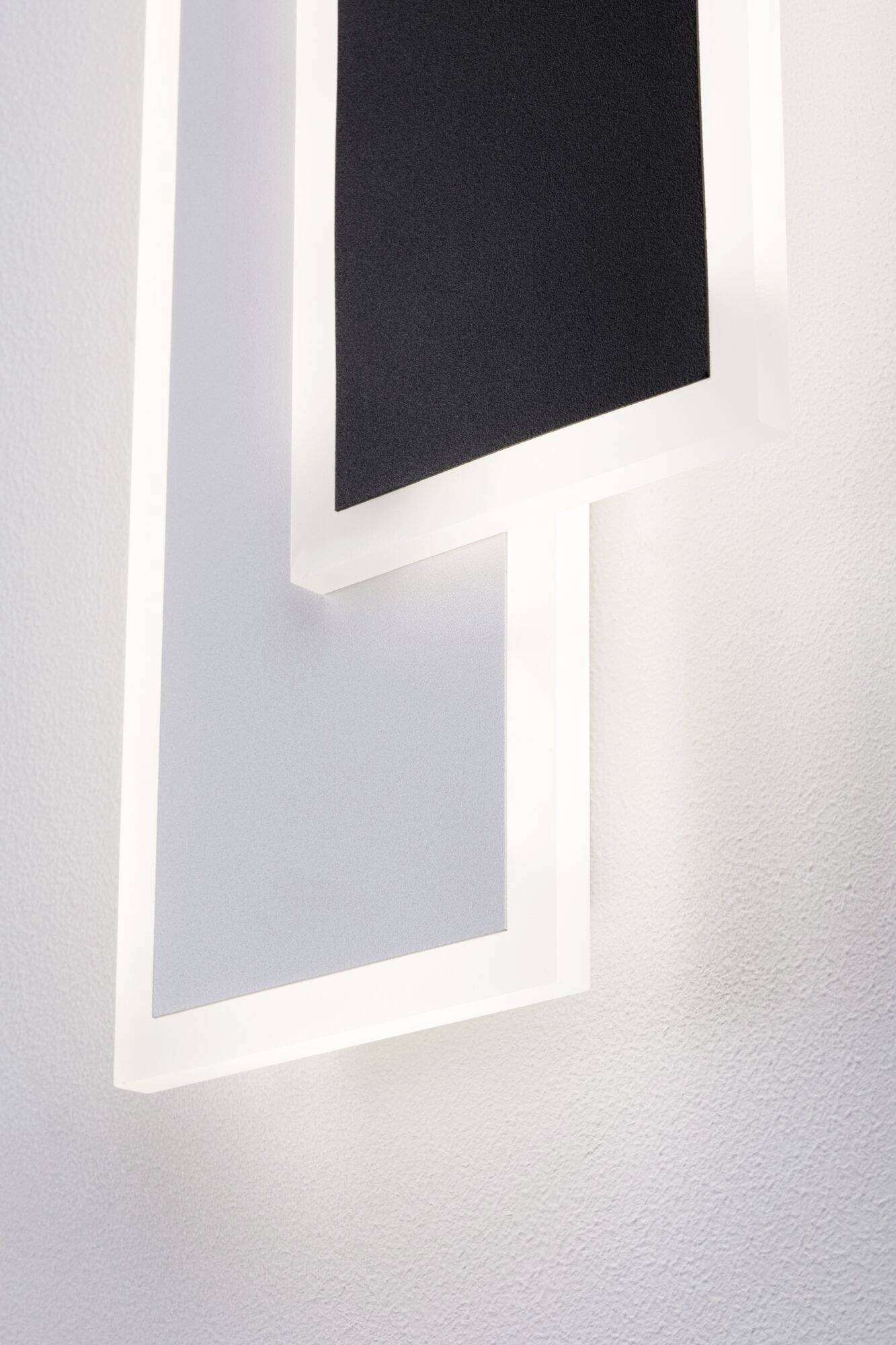 Ein Wandbild mit geometrischen Formen, hauptsächlich rechteckige und schwarze, die aufeinander gelegt sind, vor einer weißen Wand.