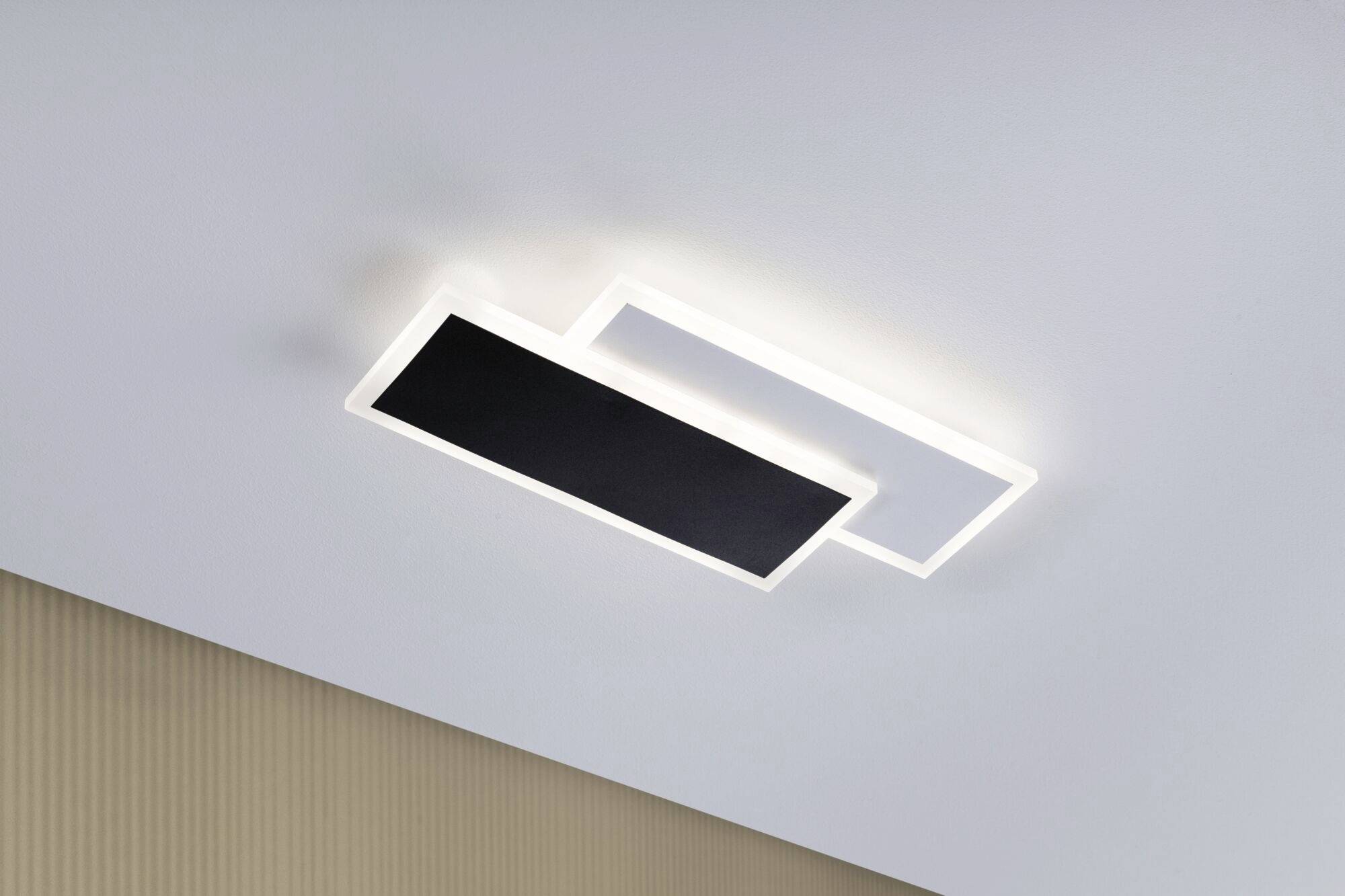 Moderne Deckenleuchte mit rechteckigem, schwarzem und transparenterem Element, gibt weiches Licht ab und ist an einer hellen Decke montiert.