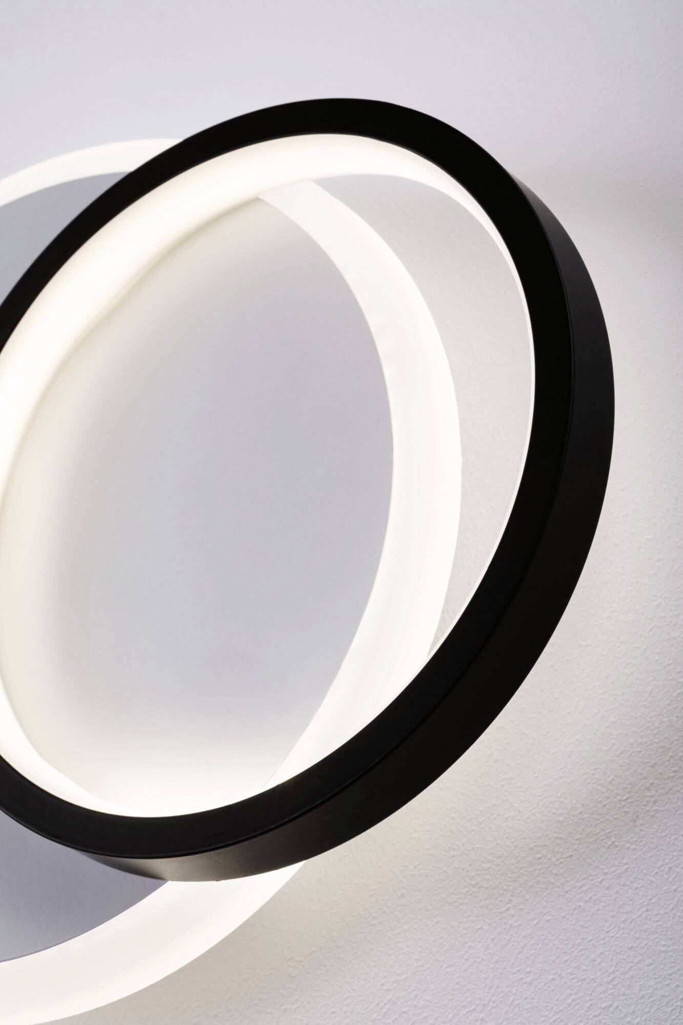 Eine moderne runde Lampe mit einem schwarzen Rahmen und einer weißen, leuchtenden Innenseite ist an einer hellen Wand montiert.