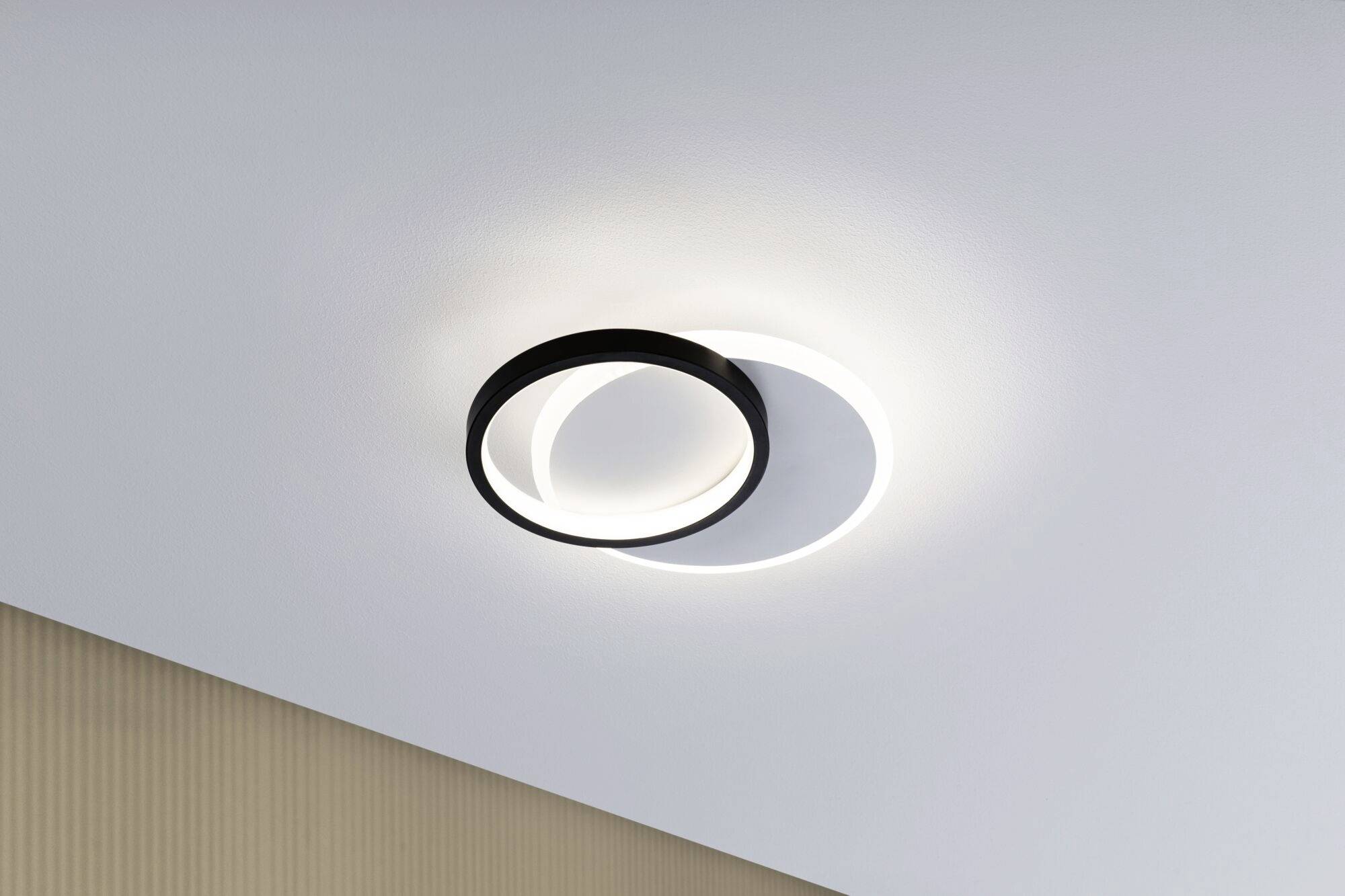 Eine moderne, runde Deckenleuchte mit schwarzem Rahmen und indirekter Beleuchtung an weißer Decke, strahlt diffuses Licht aus.