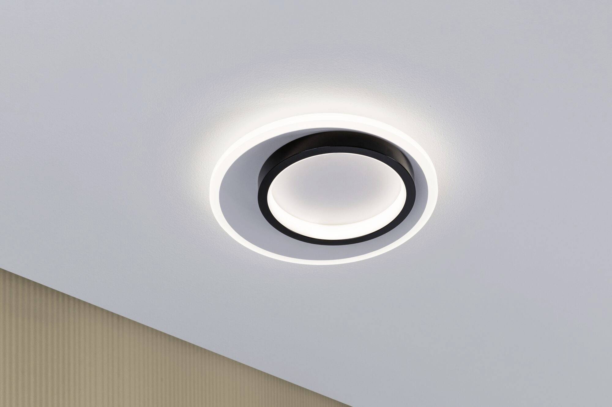 Eine moderne, kreisförmige Deckenleuchte mit schwarzem Rand und LED-Beleuchtung, montiert an einer weißen Decke.