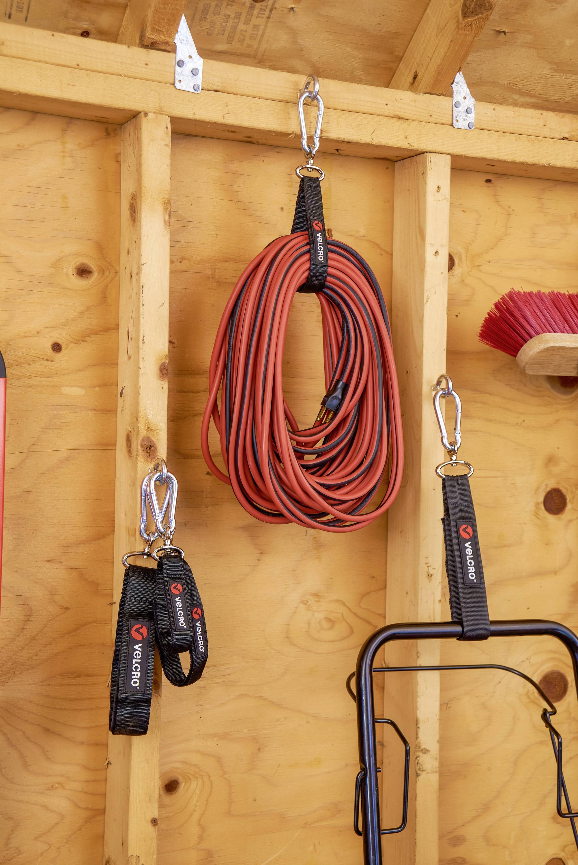 Eine Garage-Wand zeigt eine aufgerollte rote Verlängerungsschnur, die an einem Haken hängt, daneben eine rote Bürste über einem Regal.