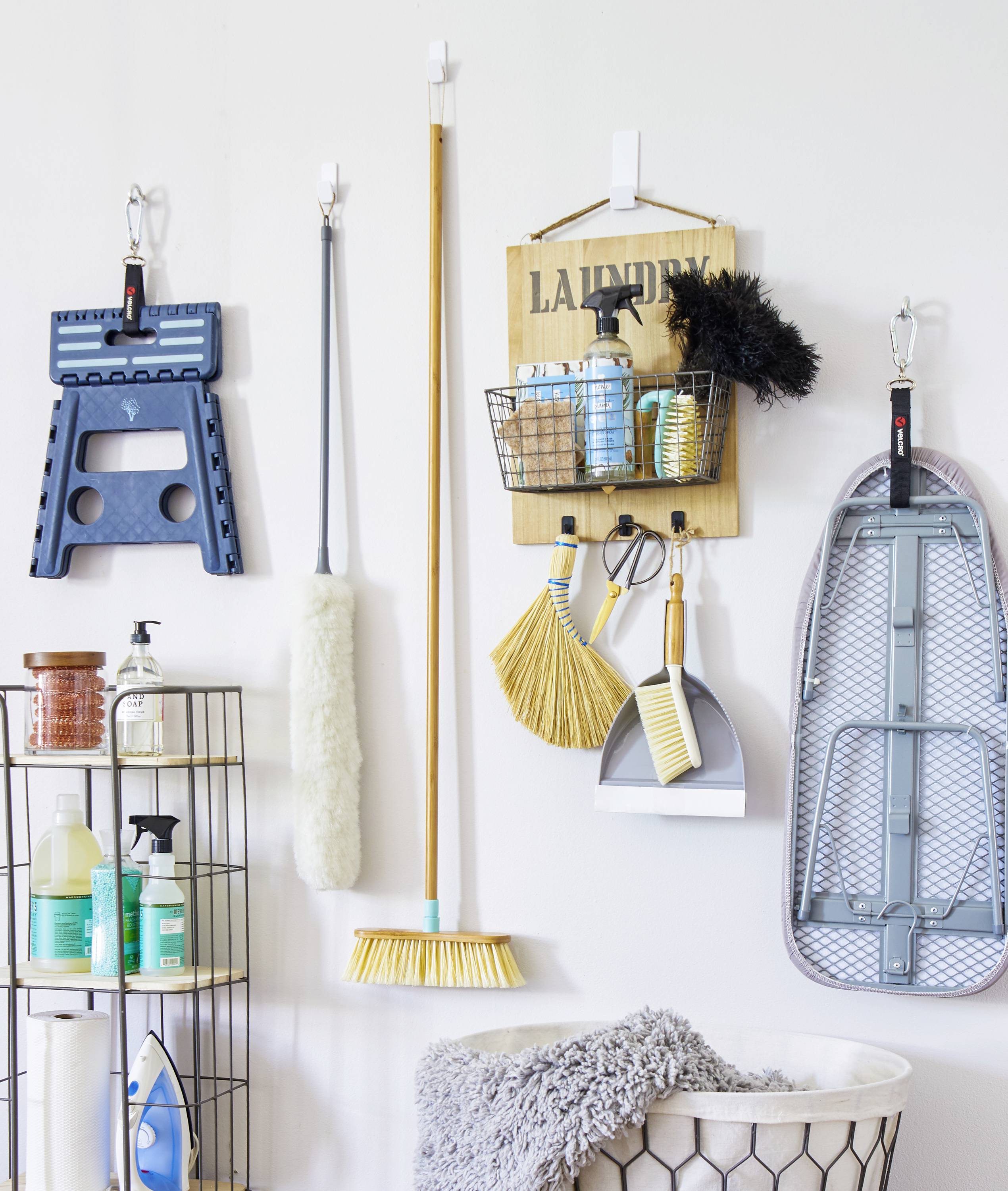 Reinigungsartikel an einer Wand organisiert: Staubsauger, Putzmittel, Besen, Kehrschaufel und ein Schild mit der Aufschrift 'Laundry'.