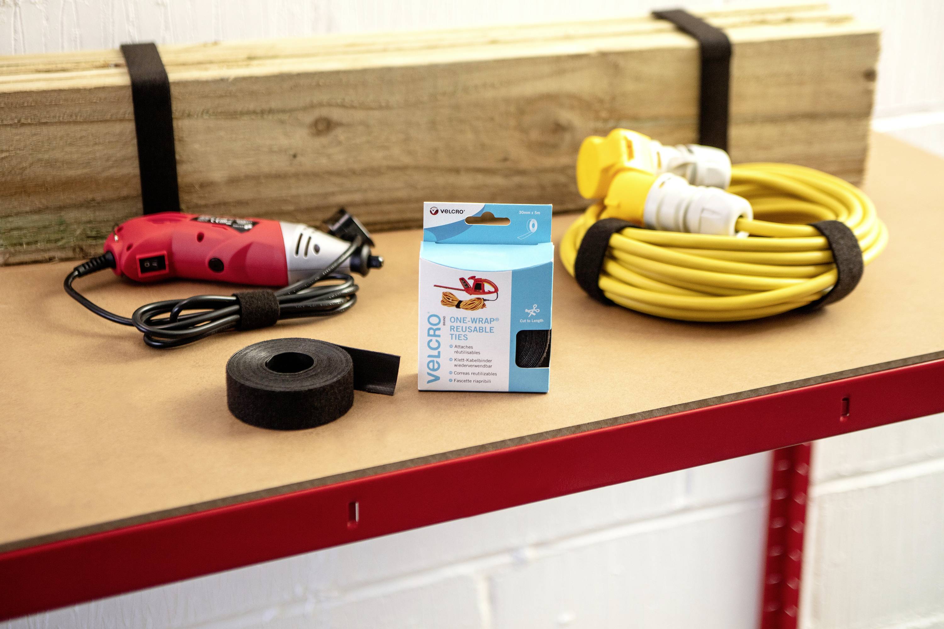 'Werkbank mit Holzbalken, Kabeltrommel, Klettbandrolle und verpacktem Klettband. Links ein rotes Elektrowerkzeug.'