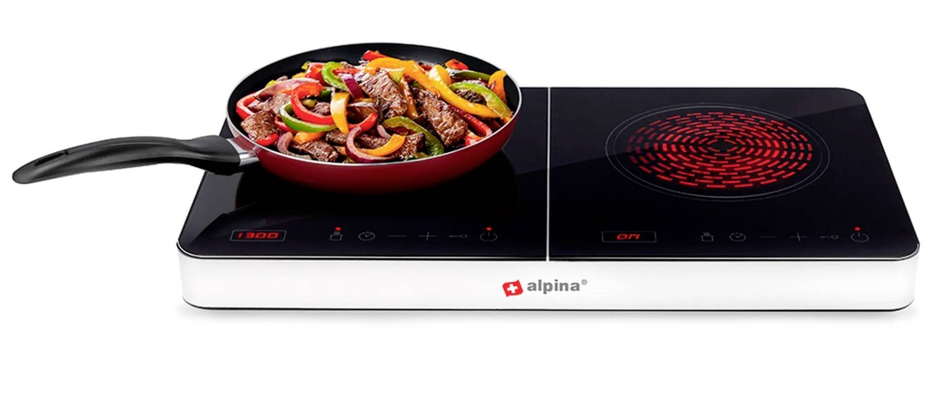 Kochplatte mit Pfanne, gefüllt mit buntem Gemüse und Fleisch. Die Platte zeigt leuchtende Kontrollleuchten an. Marke 'alpina'.
