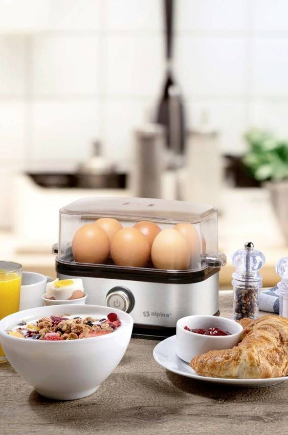 'Küche mit einem Eierkocher voller Eier, Müsli-Schale, Croissant, Saft und Gewürzen auf einem Tisch.'