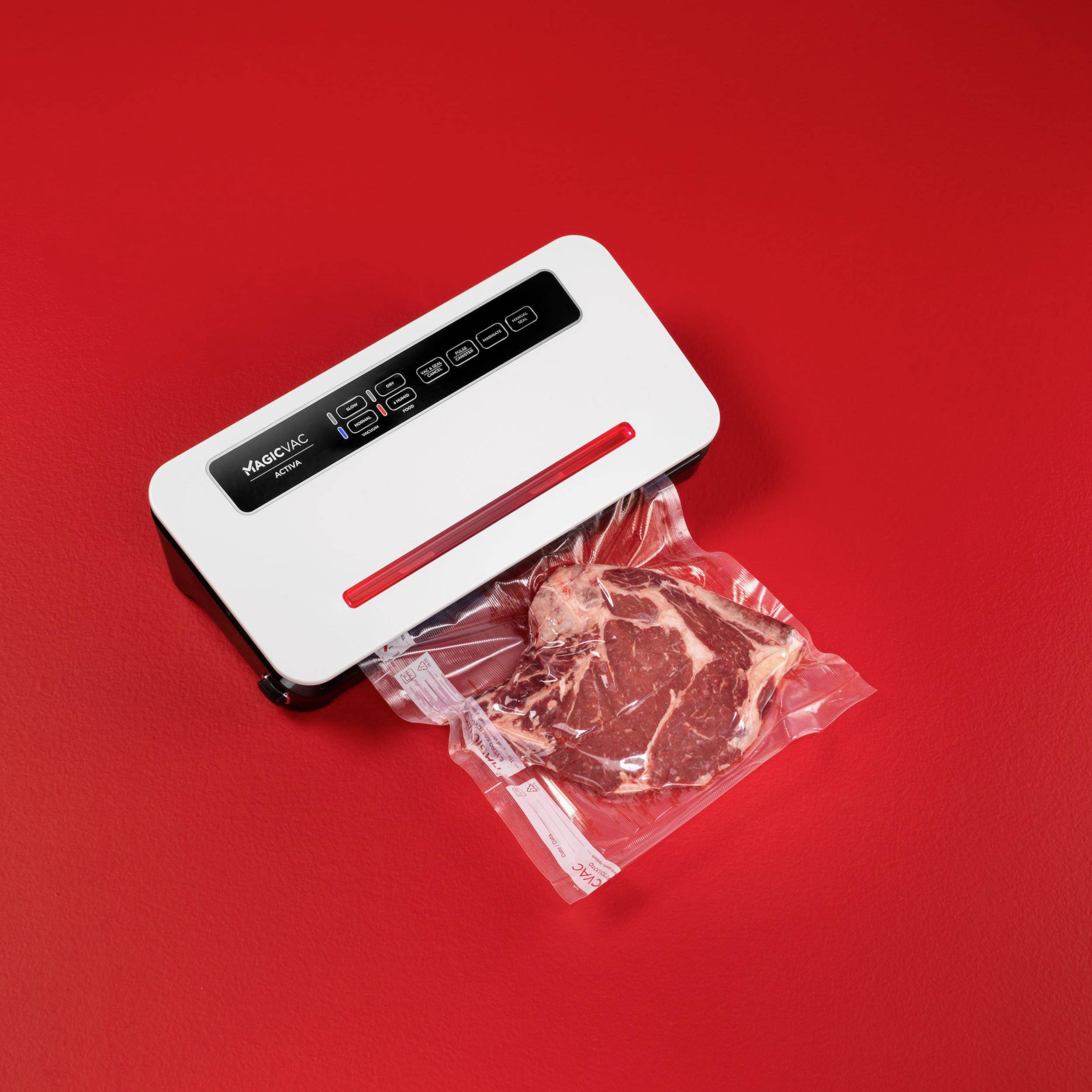 Ein Vakuumiergerät auf rotem Hintergrund vakuumiert ein Stück rohes Fleisch in einem transparenten Plastikbeutel.