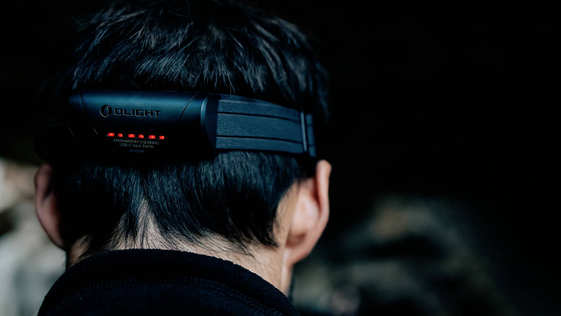 Eine Person mit kurzem dunklem Haar trägt eine Kopflampe im Dunkeln. Die Lampe hat leuchtende LED-Anzeigen auf der Rückseite.