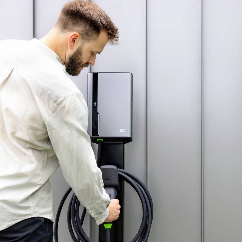 Ein Mann steckt ein Ladekabel in eine Elektroautoladestation an einer Wand ein. Empfangsbereich ist modern gestaltet.