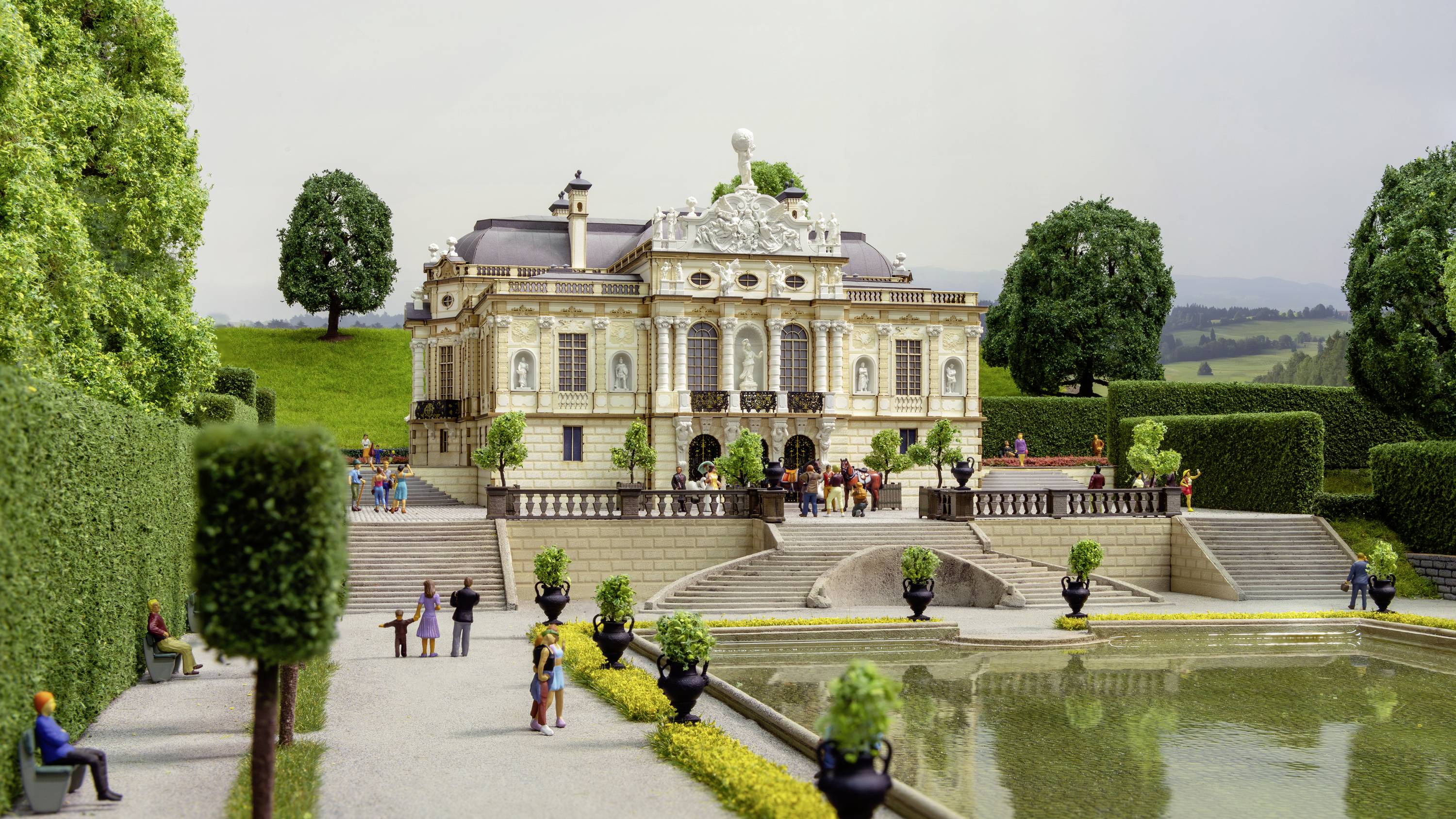 Eine Miniaturnachbildung eines Barockschlosses mit Menschen im Garten. Der Schlosspark ist symmetrisch gestaltet und gut gepflegt.