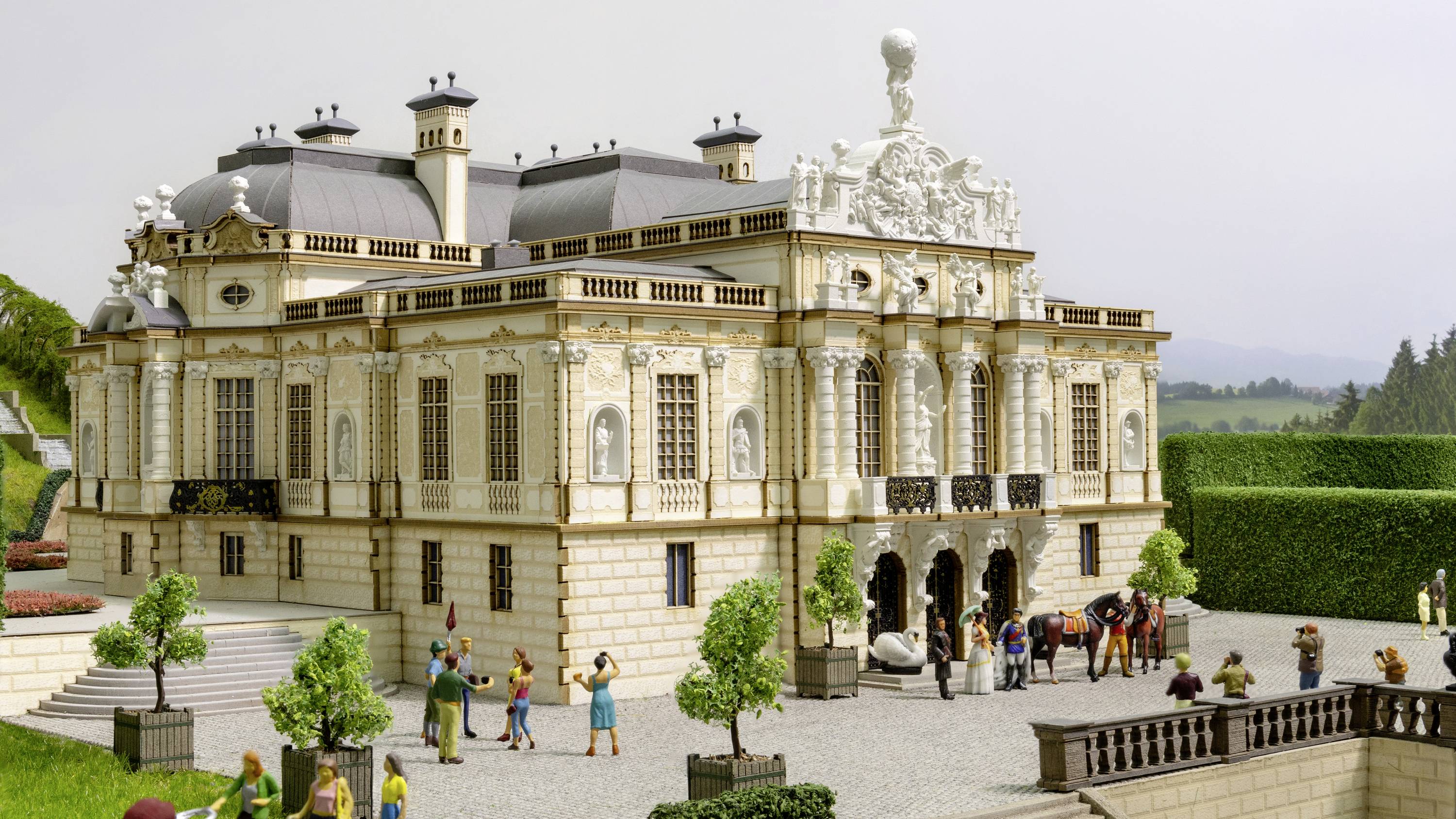 Ein detailliertes Miniaturmodell eines barocken Palastes mit Menschenfiguren im Vordergrund, das eine historische Szene darstellt.