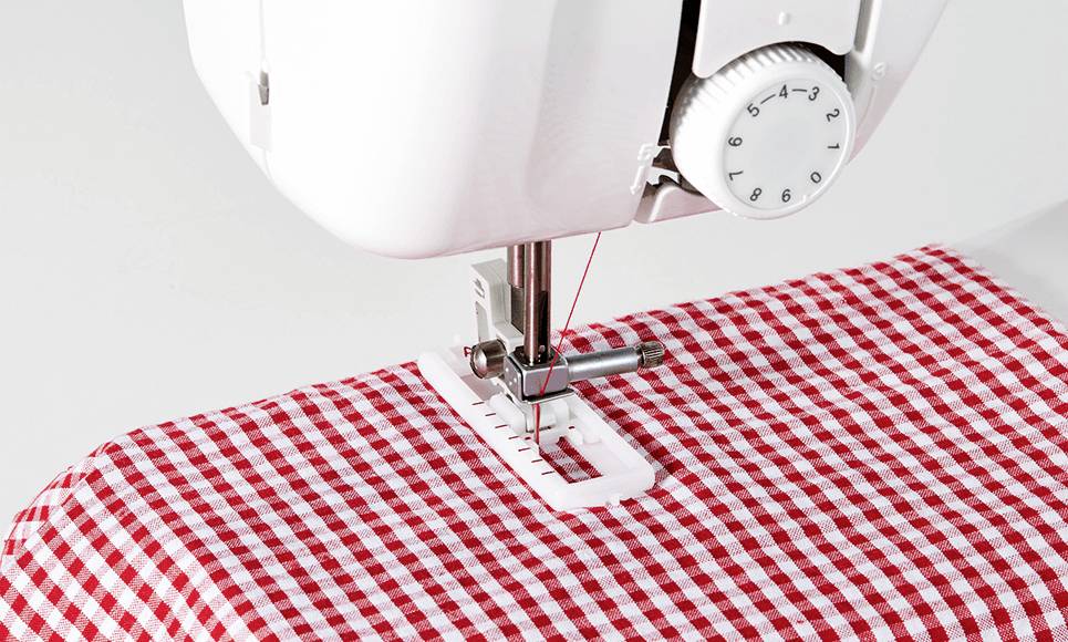 Eine Nähmaschine näht ein Knopfloch in roten und weißen karierten Stoff.