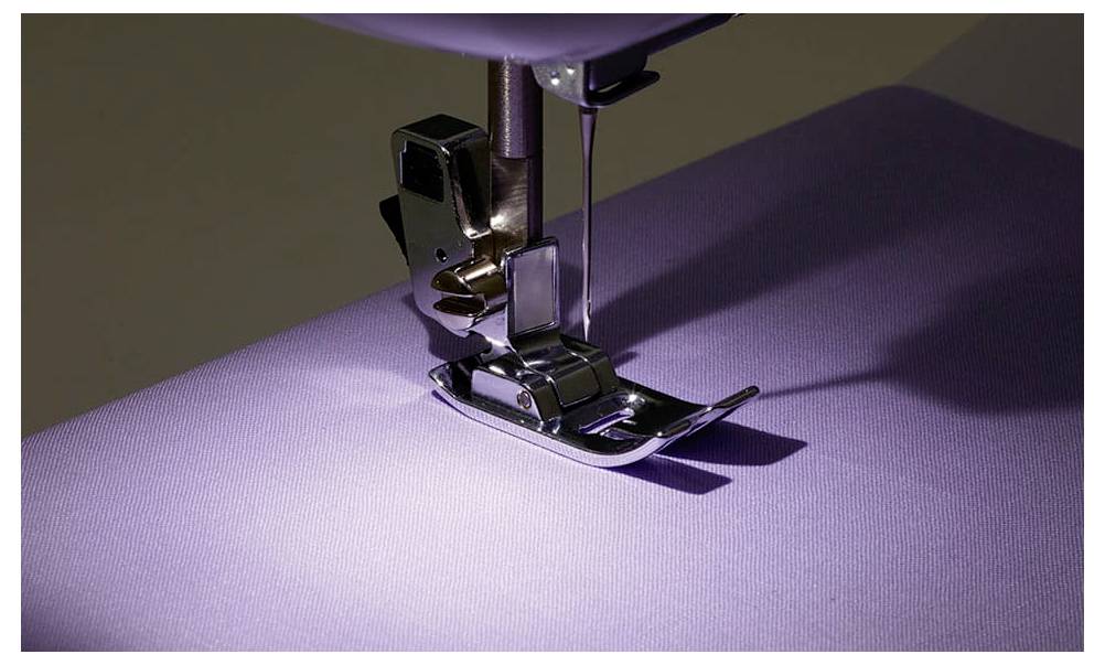 Nahaufnahme einer Nähmaschine, die lila Stoff näht. Die Nadel ist im Stoff, und das Nähfüßchen hält den Stoff in Position.