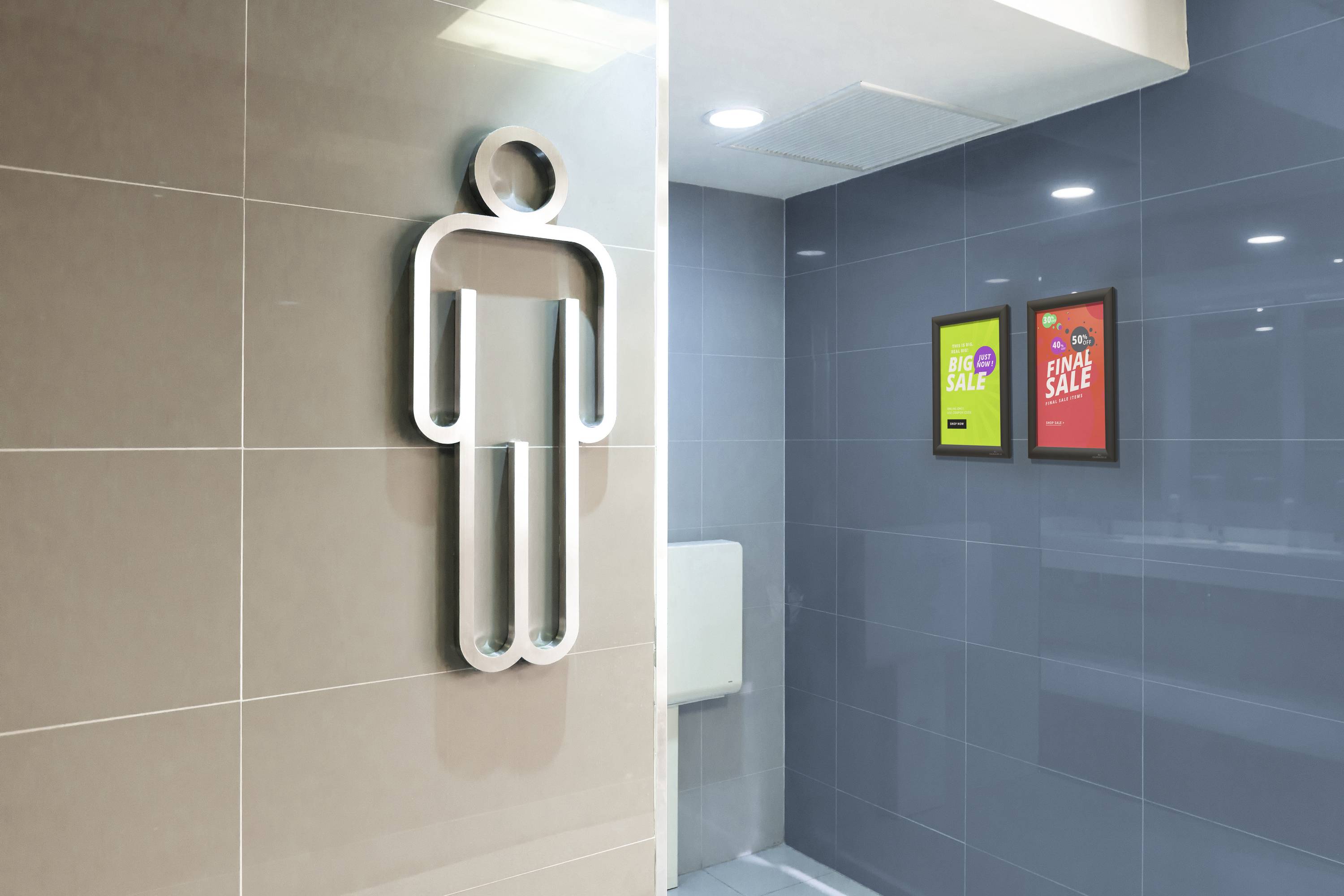 Symbol einer Herrentoilette an einer Wand; daneben zwei Werbeplakate mit Aufschriften 'BIG SALE' und 'END SALE'.