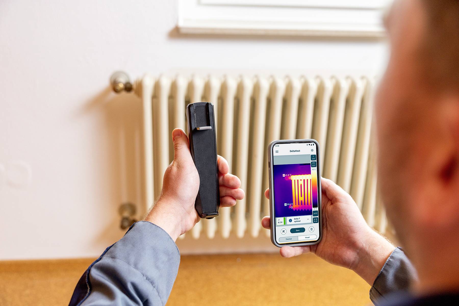 Eine Person misst mit einem Wärmebildscanner die Temperatur eines Heizkörpers. Auf einem Smartphone wird das Wärmebild angezeigt.