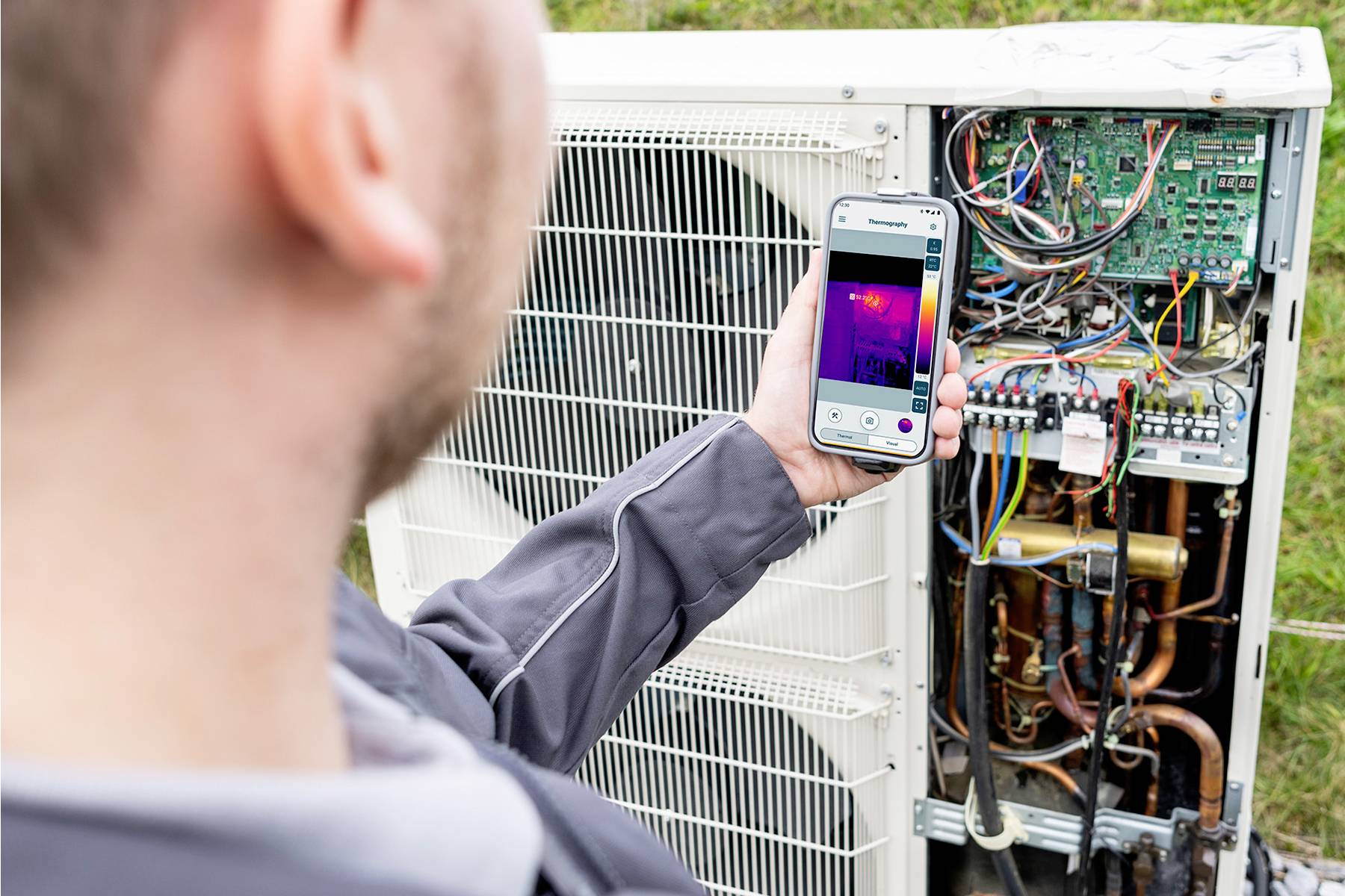 Ein Techniker verwendet ein Smartphone mit Wärmebild-App zur Diagnose eines offenen Klimageräts, um Funktionsstörungen zu erkennen.
