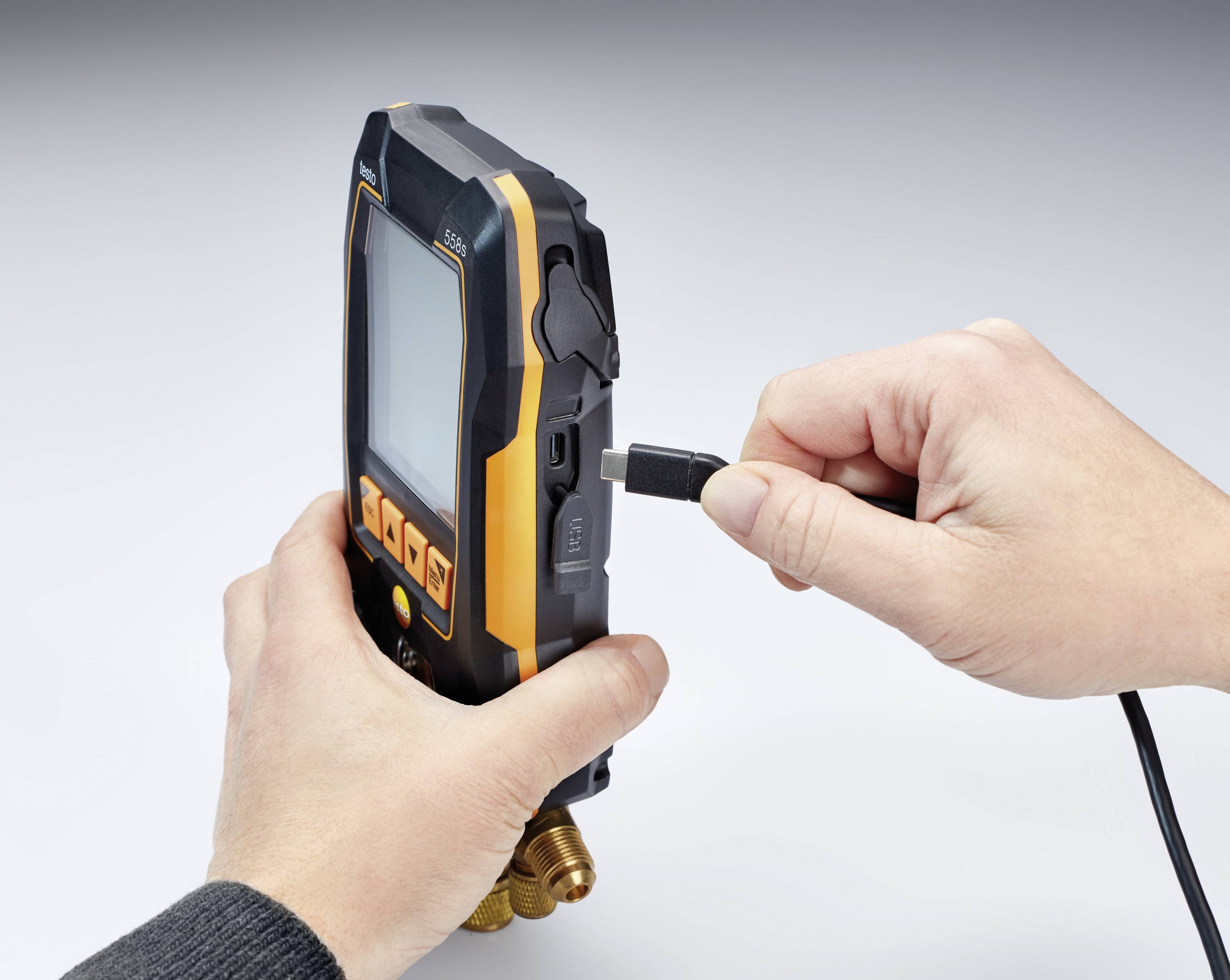 Eine Person steckt ein Kabel in ein Messgerät. Das Gerät hat ein digitales Display und ist schwarz mit orangen Akzenten.