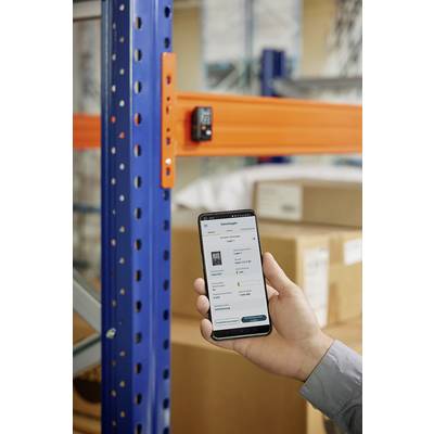 Eine Person hält ein Smartphone vor Regalen im Lager. Auf dem Bildschirm wird eine App zur Bestandsverfolgung angezeigt.