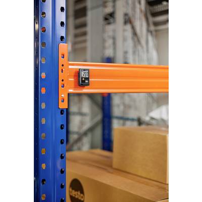 Ein Temperaturmessgerät zeigt 23,7 Grad Celsius an, angebracht an einem orangefarbenen Metallträger in einem Lager mit Pappkartons.