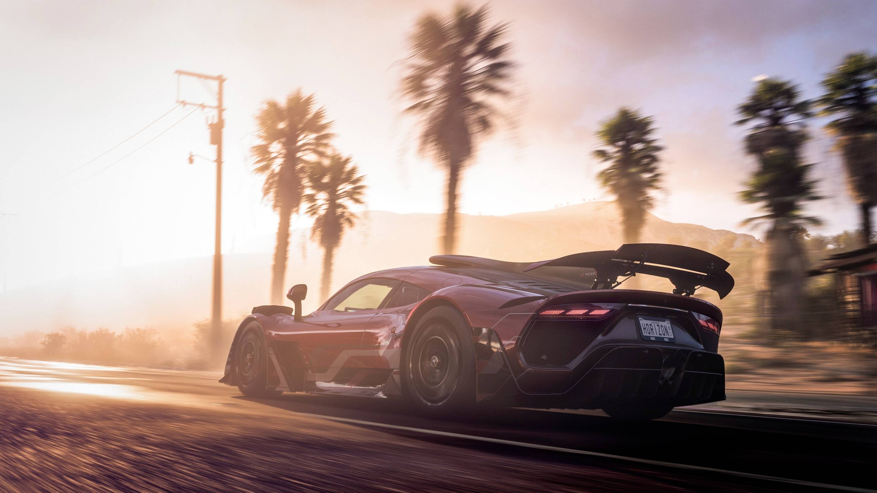 Ein Sportwagen fährt bei Sonnenuntergang eine Straße entlang, umgeben von Palmen und einem leicht bewölkten Himmel im Hintergrund.