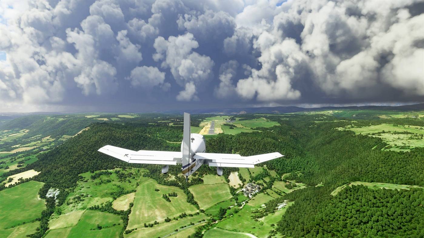 Ein kleines Flugzeug fliegt über eine grüne Landschaft in Richtung einer Landebahn, während am Horizont dunkle Wolken aufziehen.