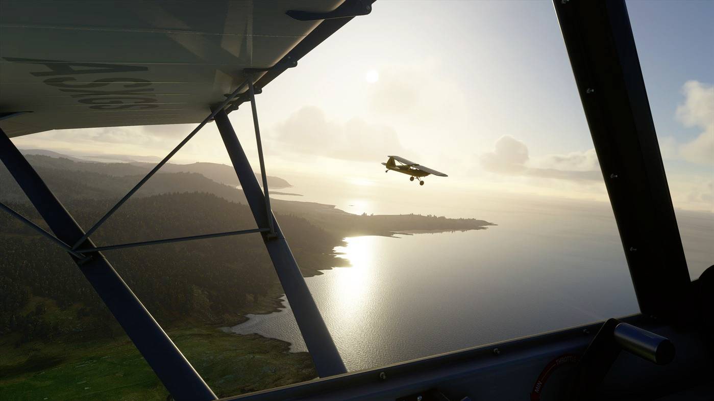 Ein kleines Flugzeug fliegt bei Sonnenuntergang über eine Küstenlandschaft. Die Ansicht ist aus der Perspektive eines anderen Flugzeugs.