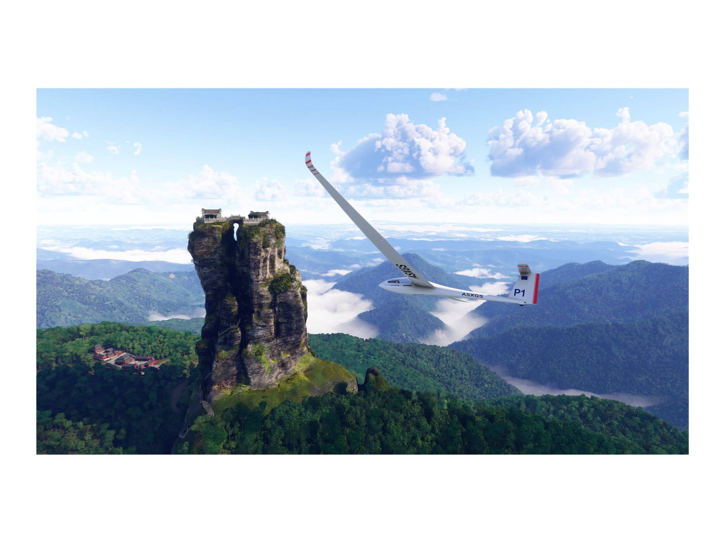 Ein Segelflugzeug fliegt über eine grüne Berglandschaft. Im Hintergrund erhebt sich ein markanter Fels mit einem kleinen Gebäude an der Spitze.