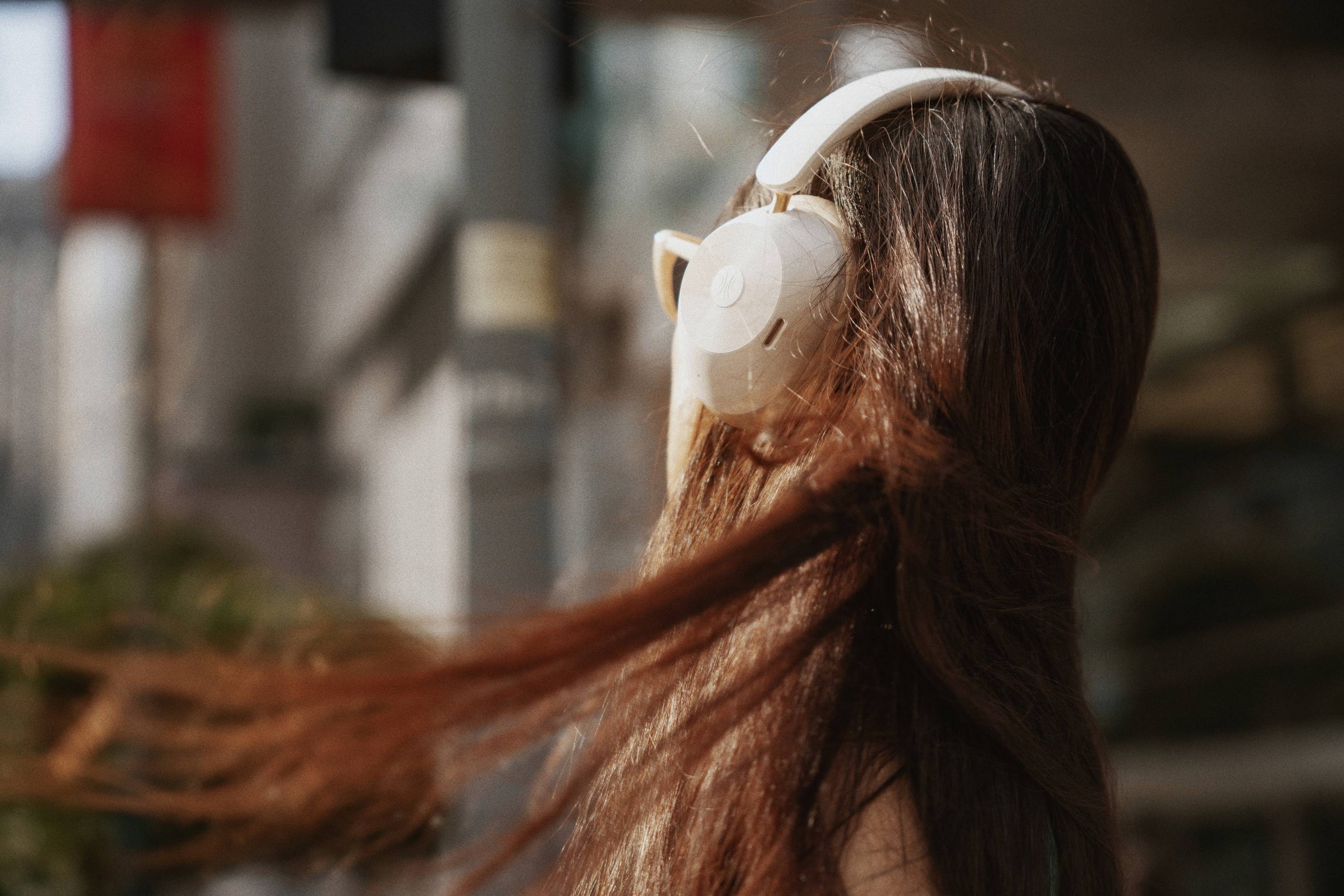 Eine Frau mit langen, wehenenden Haaren trägt große Kopfhörer und geht durch eine städtische Umgebung.